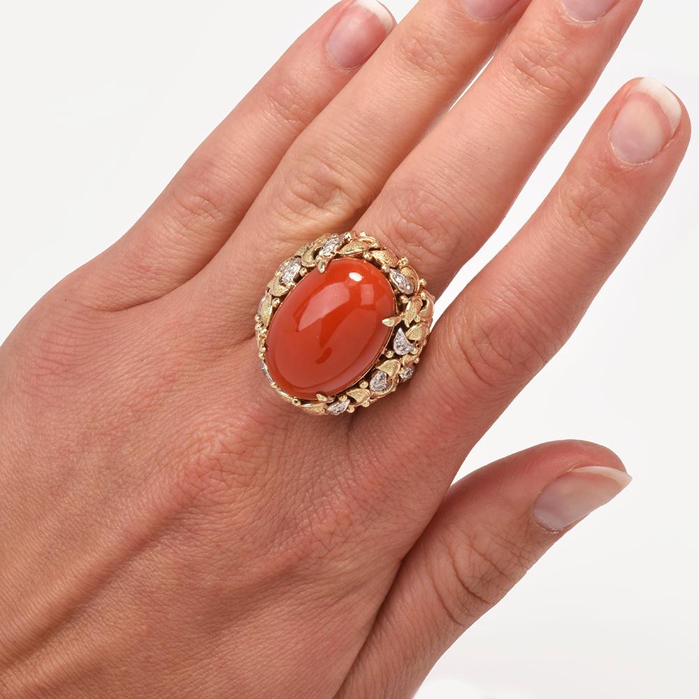 This bold circa 1970s coral and diamond is crafted with a combination of 14-karat yellow and white gold, weighing 23.6 grams and measuring 30mm x 15mm high. Centered with one prong-set oval shaped natural red coral, measuring 24mm x 17mm. Surrounded