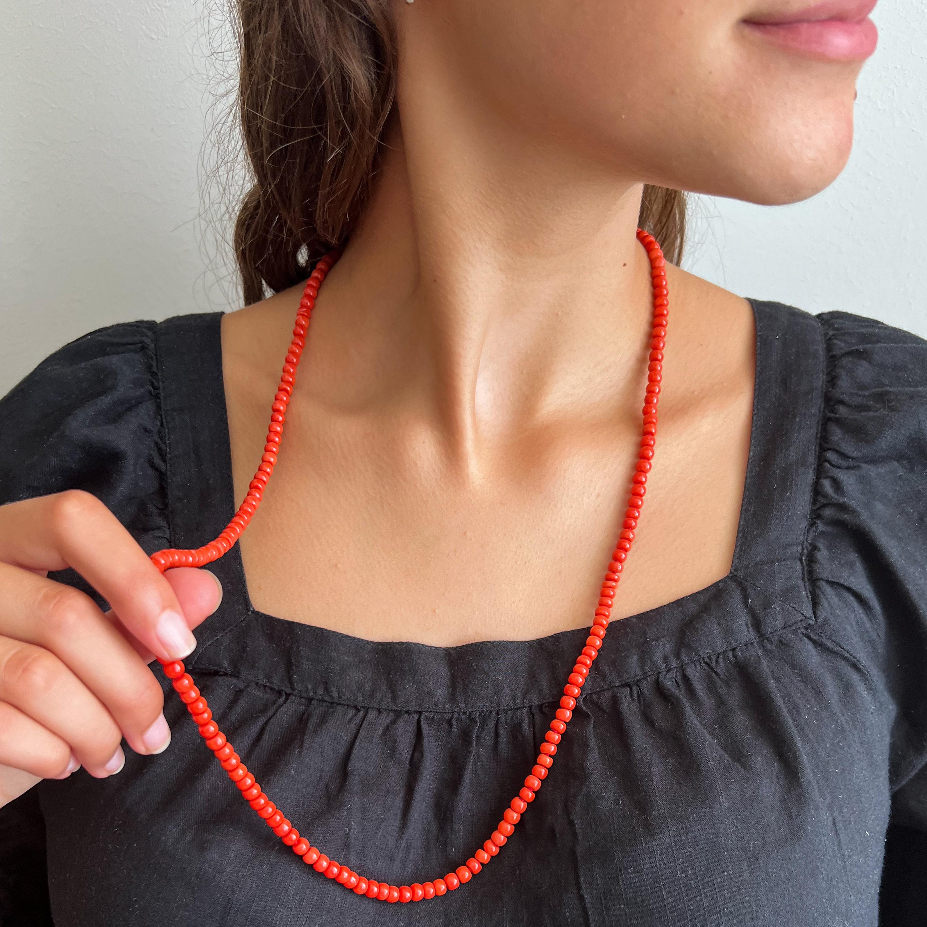A natural coral and 14 karat gold long single-strand beaded necklace. The coral beads of this necklace are barrel-shaped and set with a beautiful round-shaped clasp created in 14 karat gold. The clasp is set with a smooth round-shaped coral cabochon