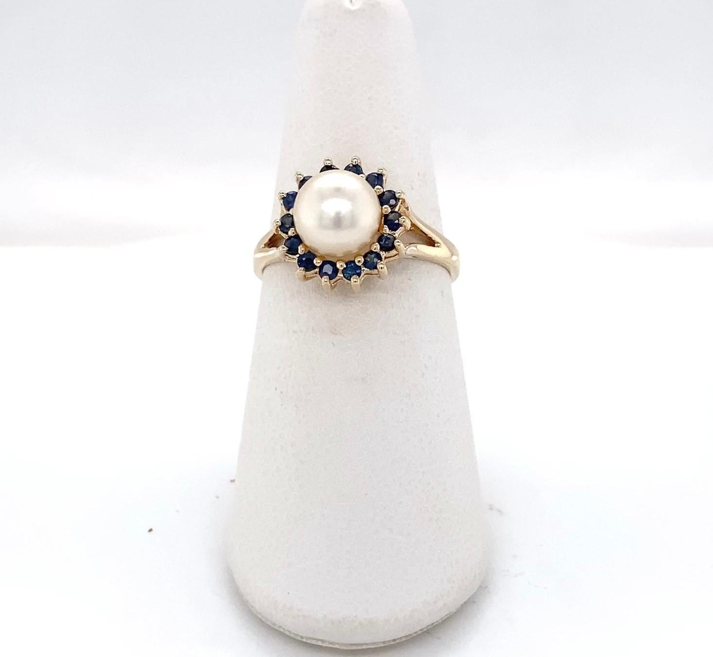 Cette bague classique de style vintage présente une perle de culture naturelle lustrée d'environ 7,6 mm encadrée d'un halo radieux de quatorze (14) saphirs de taille ronde d'un poids total d'environ 0,21 carat qui rehaussent la beauté de la perle.