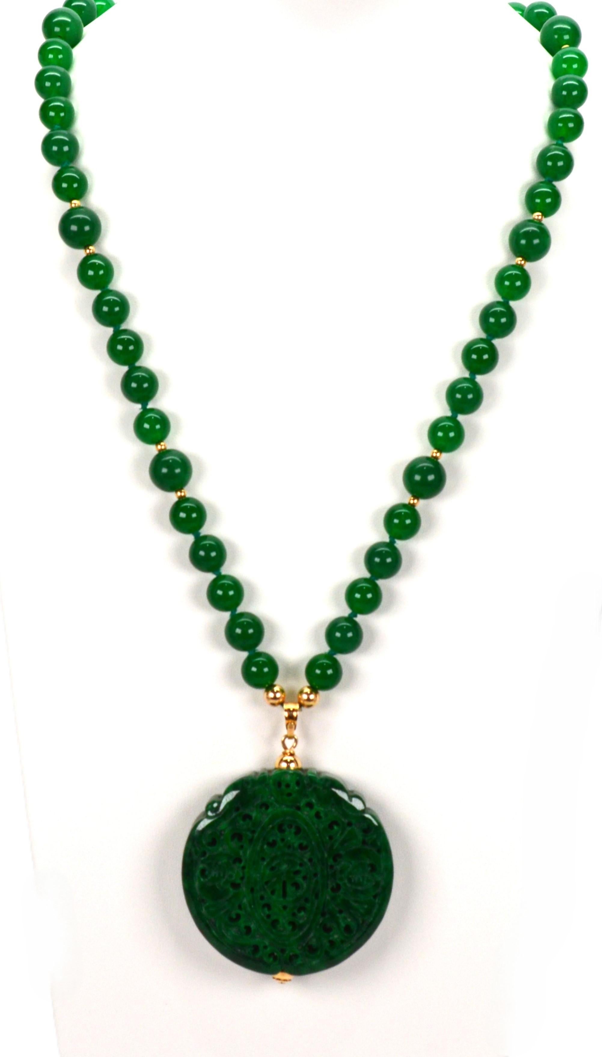 Artisan carved natural Jadeite creates this bold beaded statement necklace with medallion pendant. A 24 inch strand of  highly polished 10mm jadeite beads is hand strung and knotted with intermittently placed 12 karat yellow gold beads complimenting