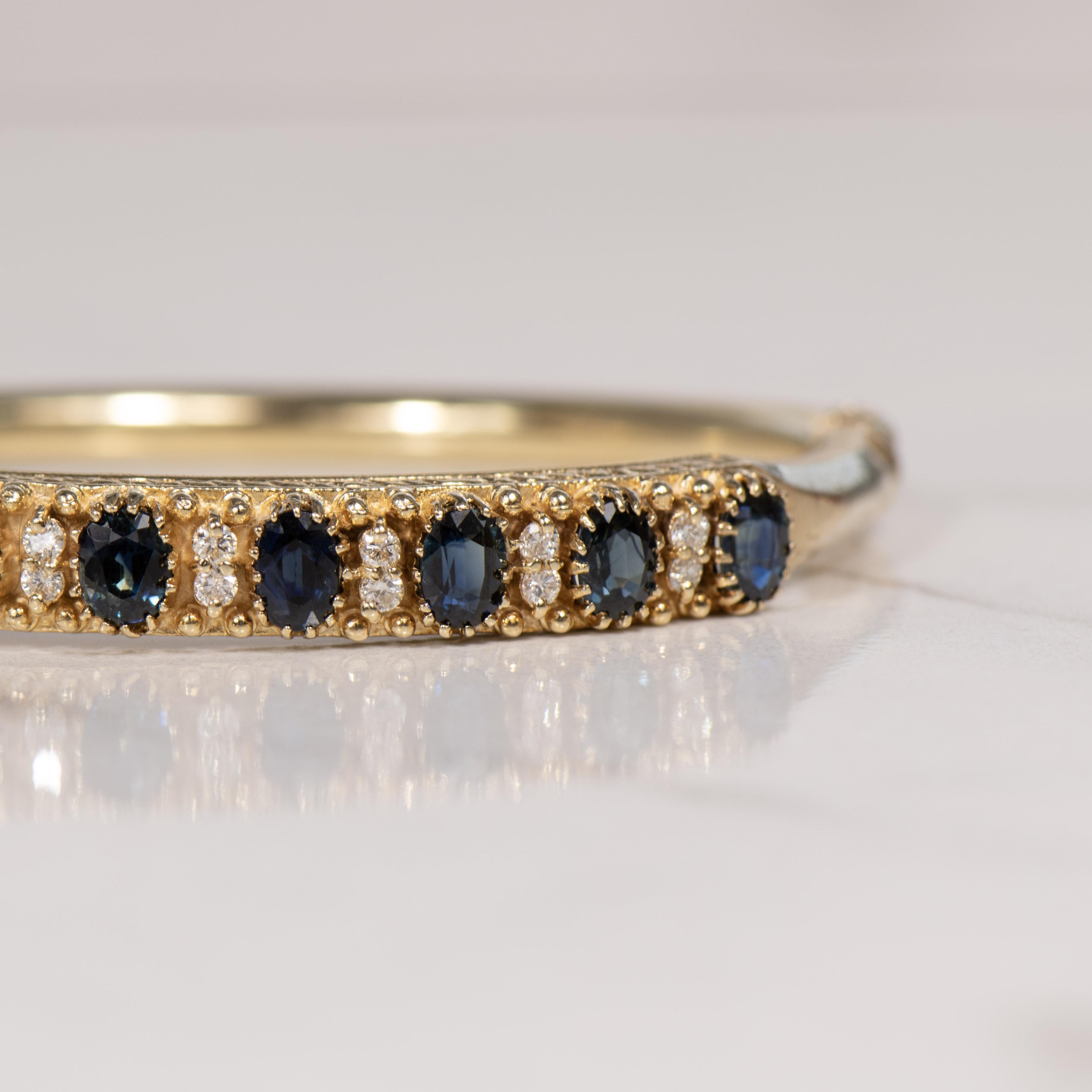 Embrace the allure of yesteryears with this exquisite 14K vintage hinged bangle, adorned with natural blue sapphires and diamonds. The bangle exudes a timeless charm, meticulously crafted in lustrous 14K gold, offering both durability and a warm,