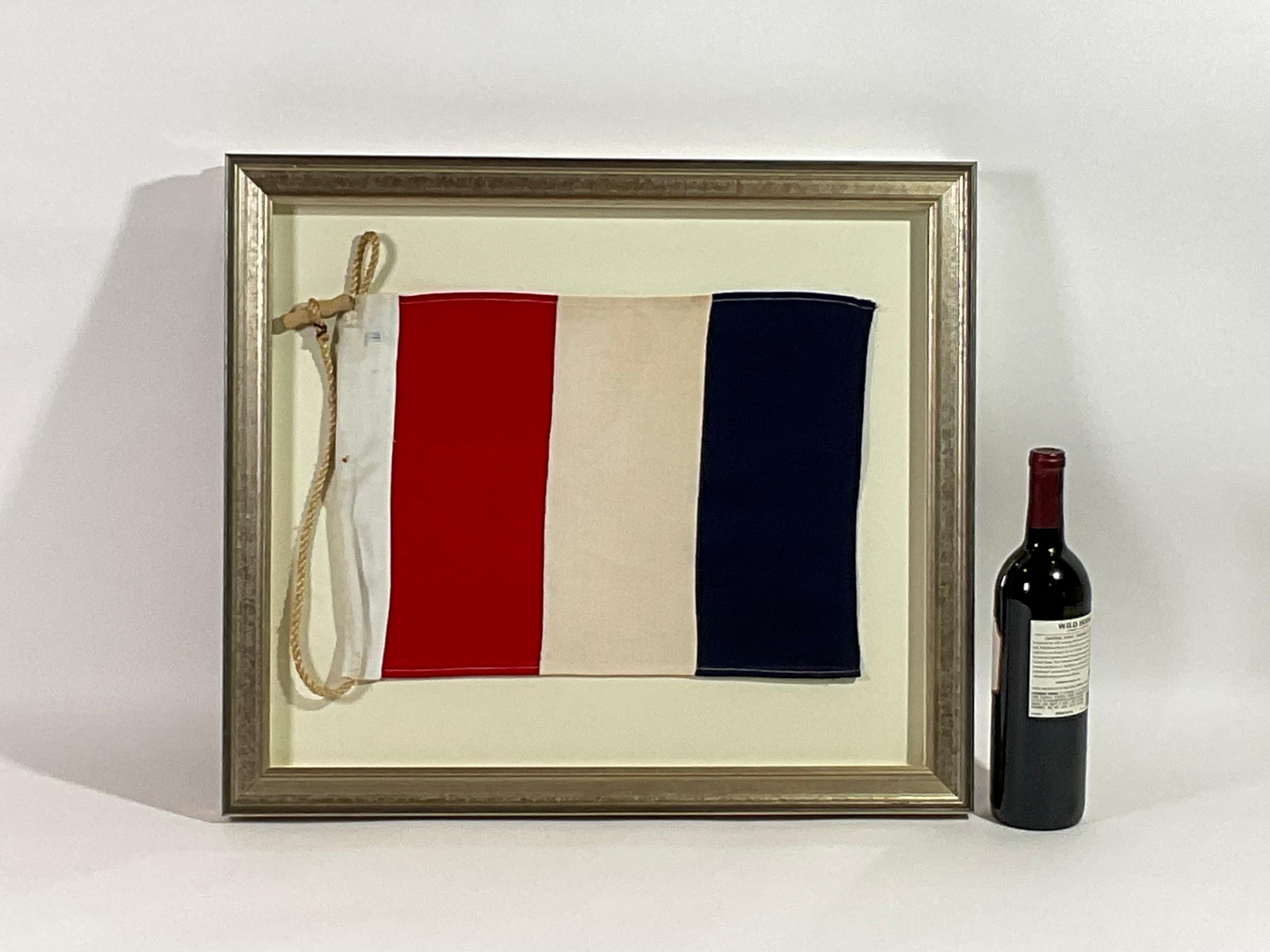 Framed maritime signal flag representing the letter “T” in the international code of signals.  This authentic pennant is made of individual panels of red, white and blue cotton. Fitted to a heavy canvas hoist band with original rope and toggle. This