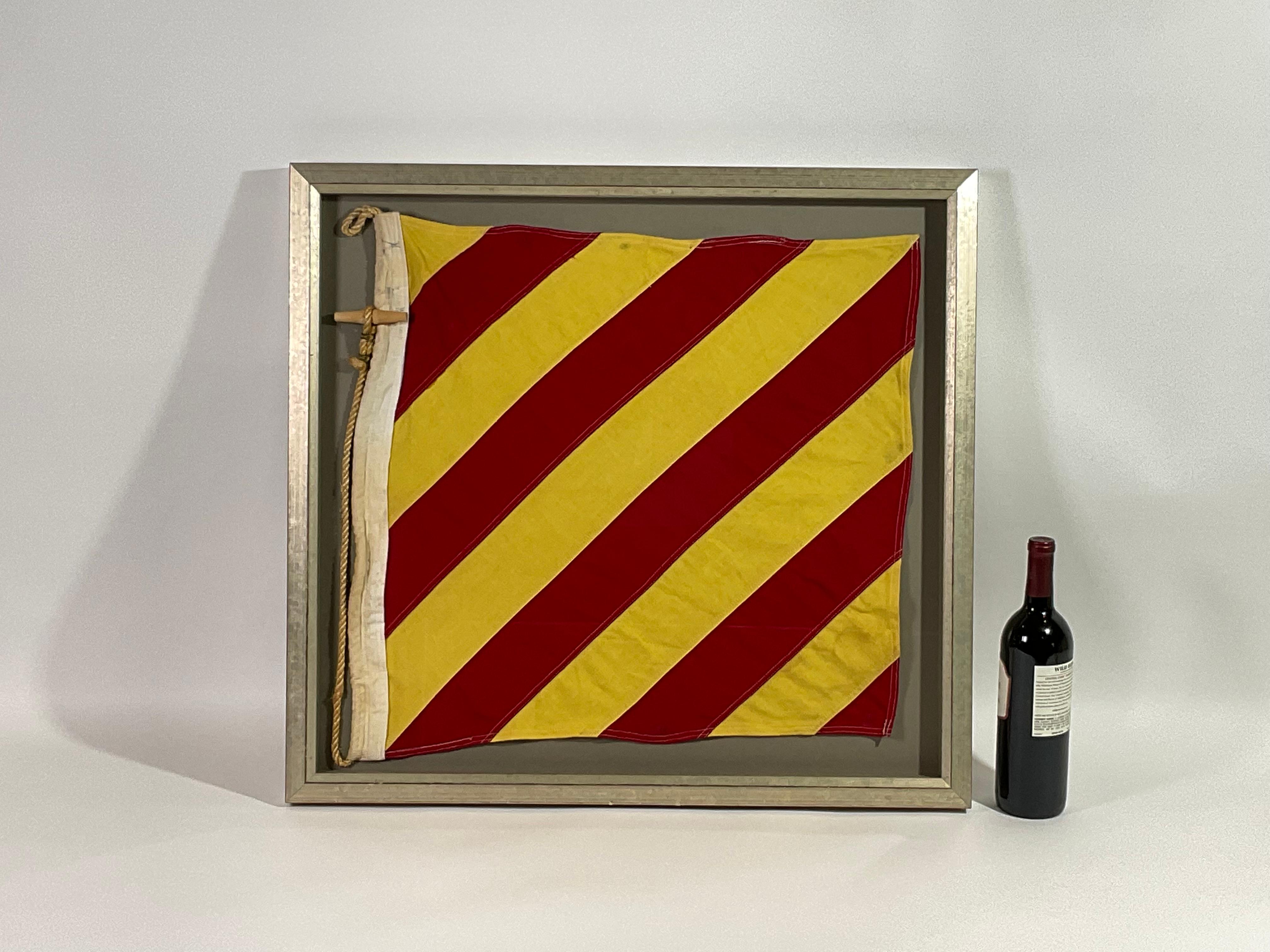 Framed maritime signal flag representing the letter “Y” in the international code of signals. This authentic and ocean used pennant is made of individual panels of red and yellow. Fitted to a heavy canvas hoist band with original rope and wood