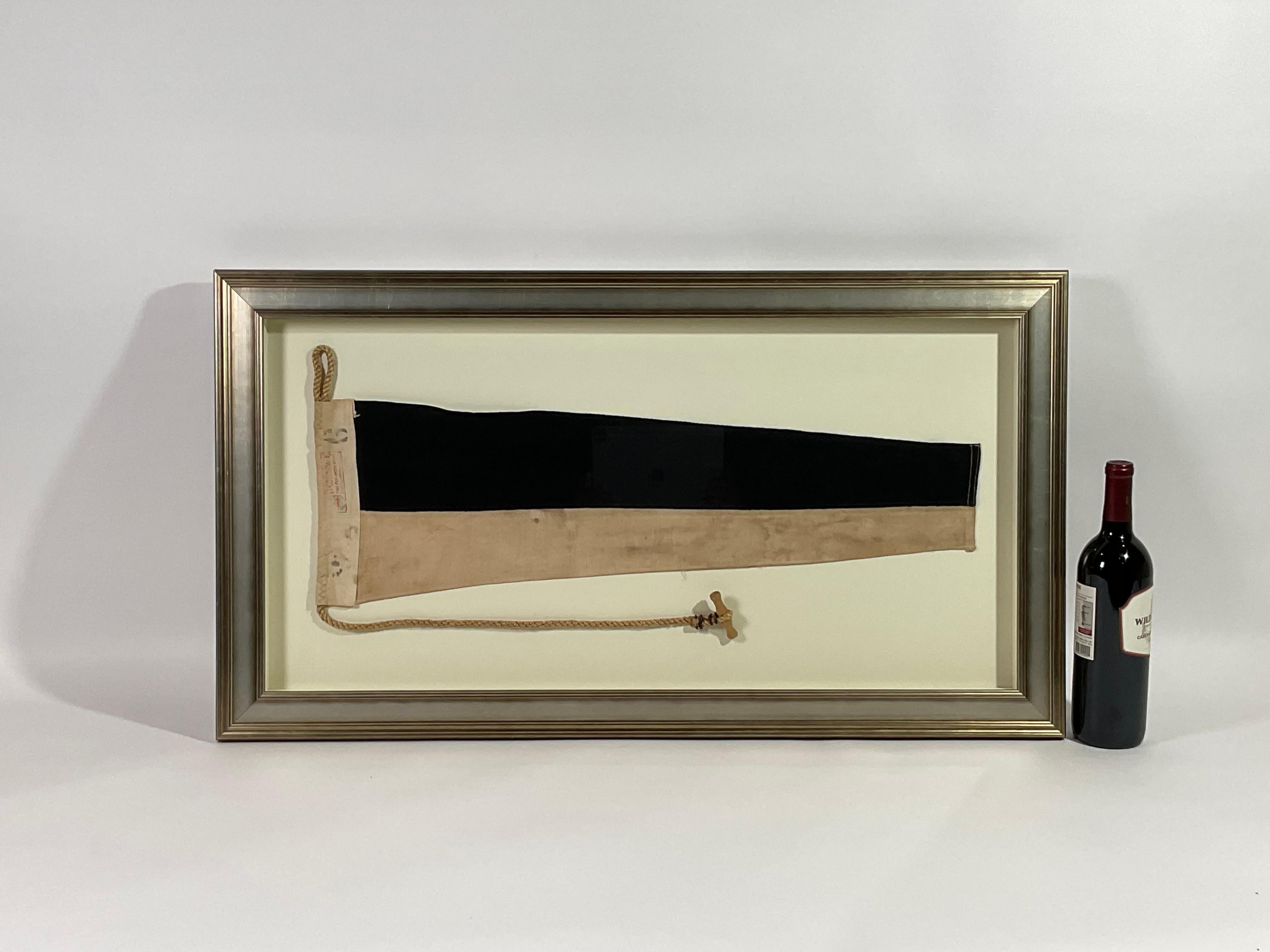 Framed maritime signal flag representing the number “6” in the international code of signals. This authentic and ocean used pennant is made of individual panels of black and white. Fitted to a heavy canvas hoist band with original rope and wood