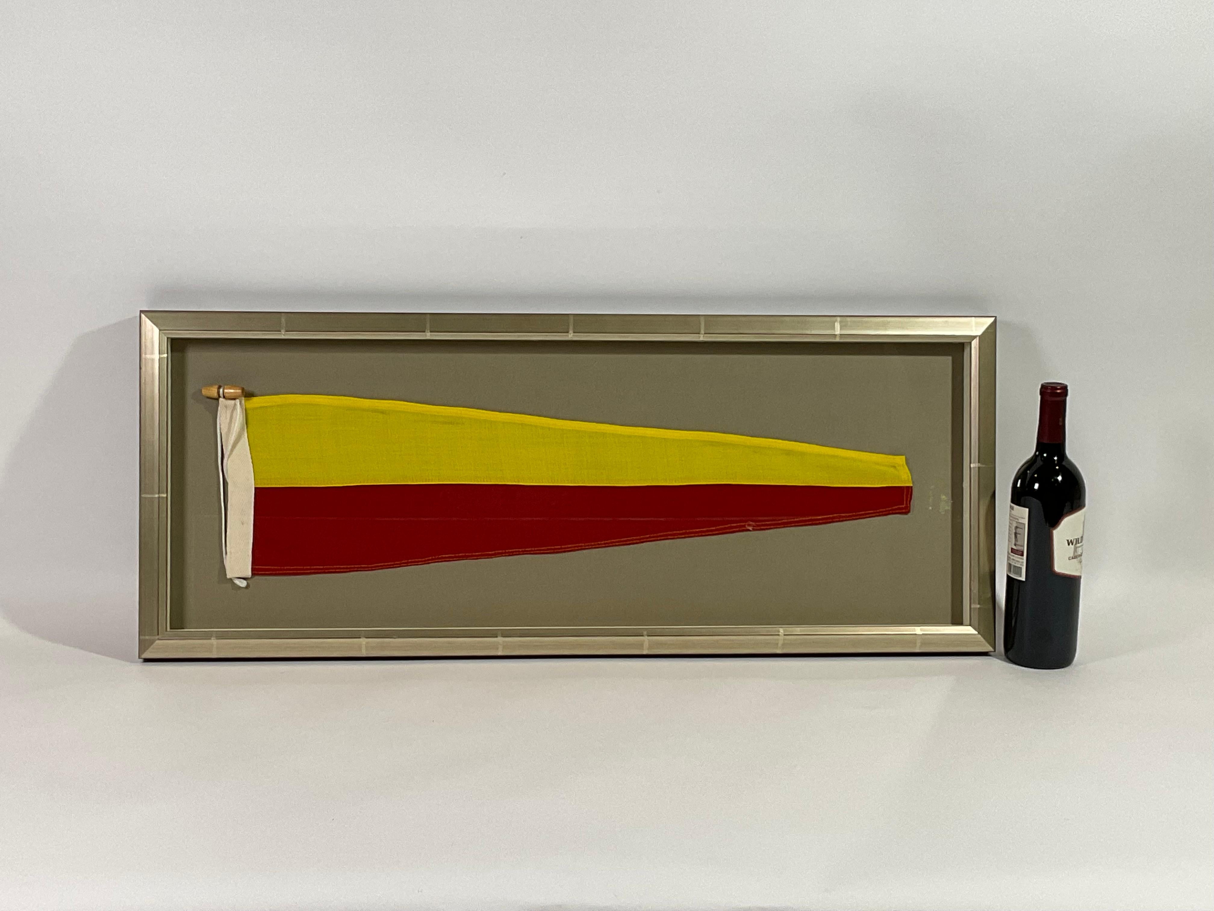 Framed maritime signal flag representing the number “7”, “SEVEN” in the international code of signals. This authentic pennant is made of individual panels of yellow and red. Fitted to a heavy canvas hoist band with original cord and wood toggle.