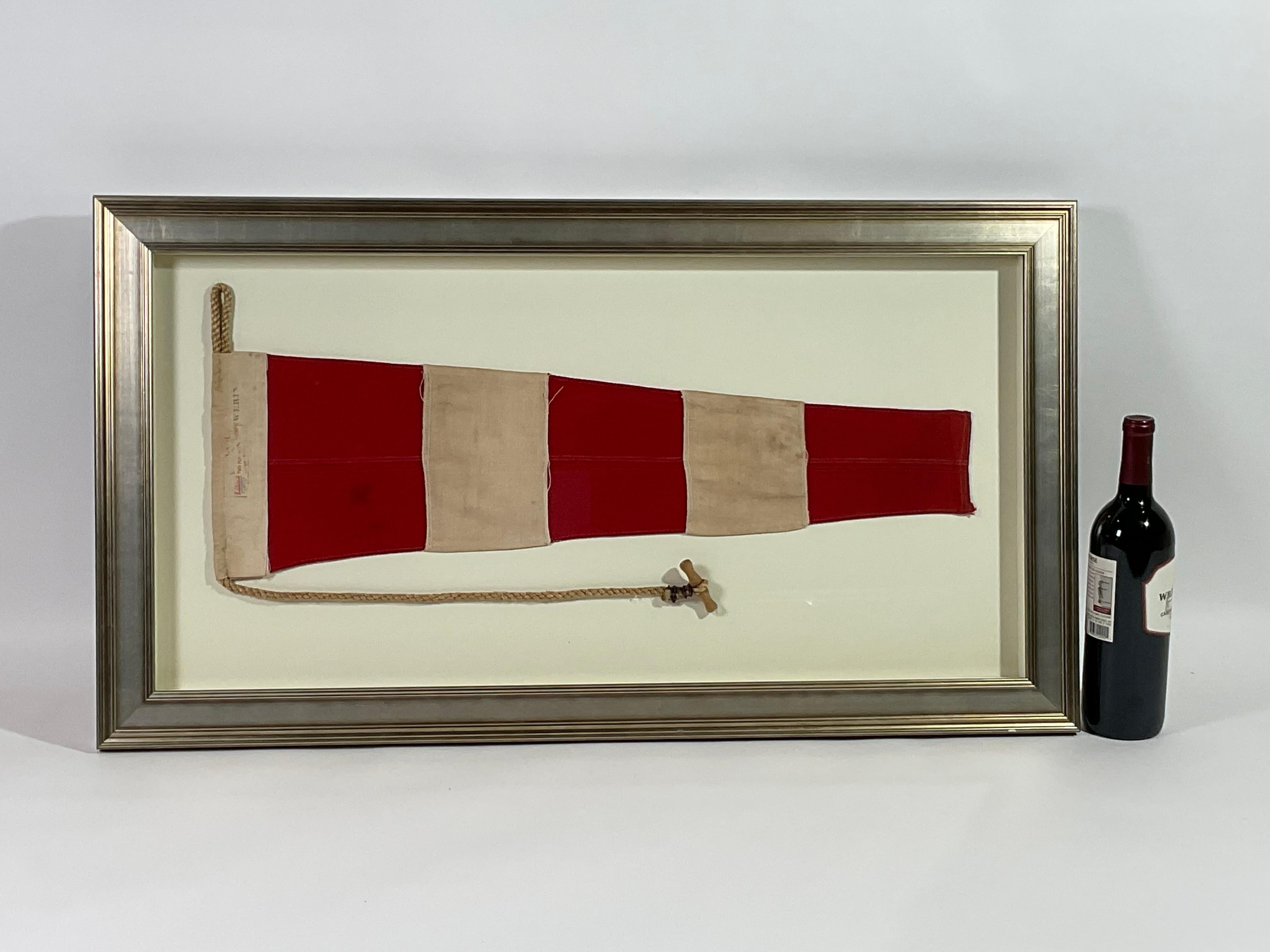 Framed maritime signal flag representing the “ANSWERING PENNANT” in the international code of signals. This authentic and ocean used pennant is made of individual panels of red and white. Fitted to a heavy canvas hoist band with original rope and