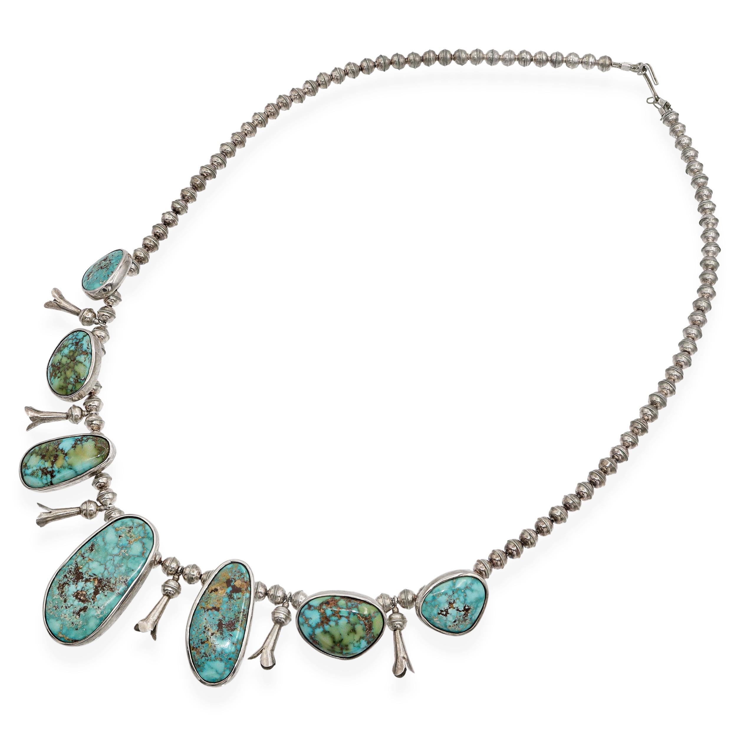 Questa collana vintage Navajo presenta sette cabochon di turchese naturale, ciascuno con motivi unici a matrice nei toni del blu e del verde, incastonati in castoni lisci d'argento. I tradizionali fiori di zucca pendono tra le pietre, simboleggiando
