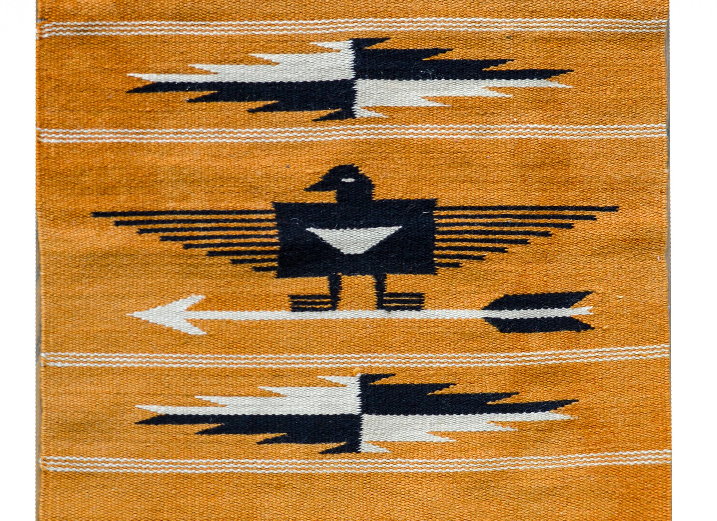 A vintage Navajo rug with large central stylized eagle standing on an arrow, and flanked by two diamond medallions, and set against a striped background woven in pink, indigo, white, and orange.