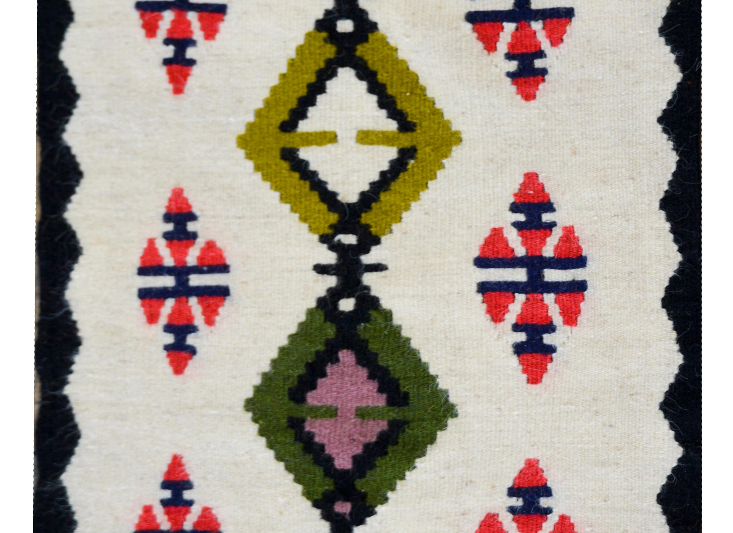 Un saisissant tapis Navajo vintage avec plusieurs diamants sur toute sa longueur et vivant au milieu d'un champ d'autres motifs de diamants, le tout tissé en cramoisi, indigo, vert, jaune moutarde et rose, et entouré d'une bordure à motifs en zigzag.