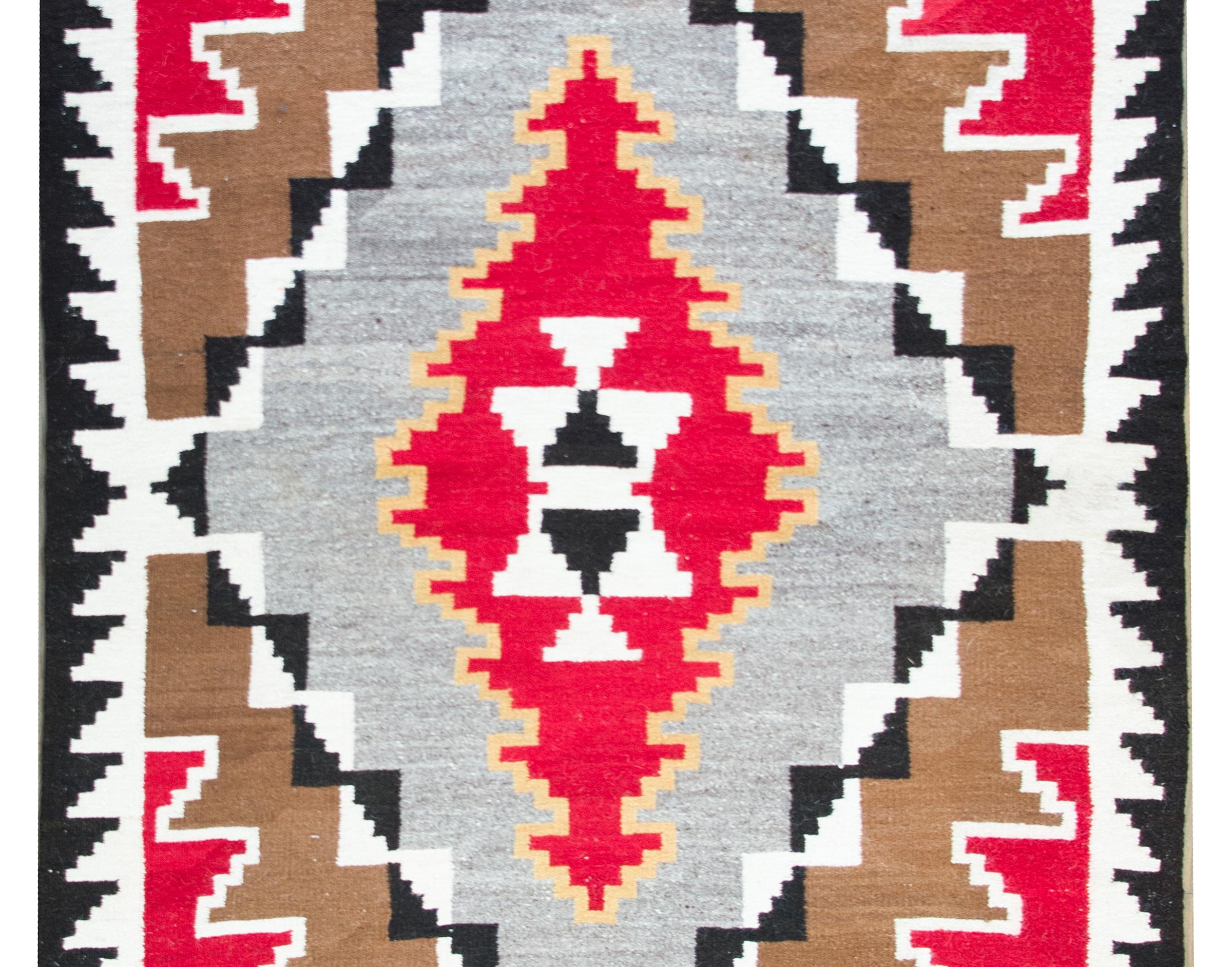Impresionante alfombra navajo vintage con un dibujo de rombos que reducen su tamaño y cambian de color, y separados por dibujos en zigzag o triángulos, todo ello tejido en lana carmesí, marrón, dorada, negra y blanca.