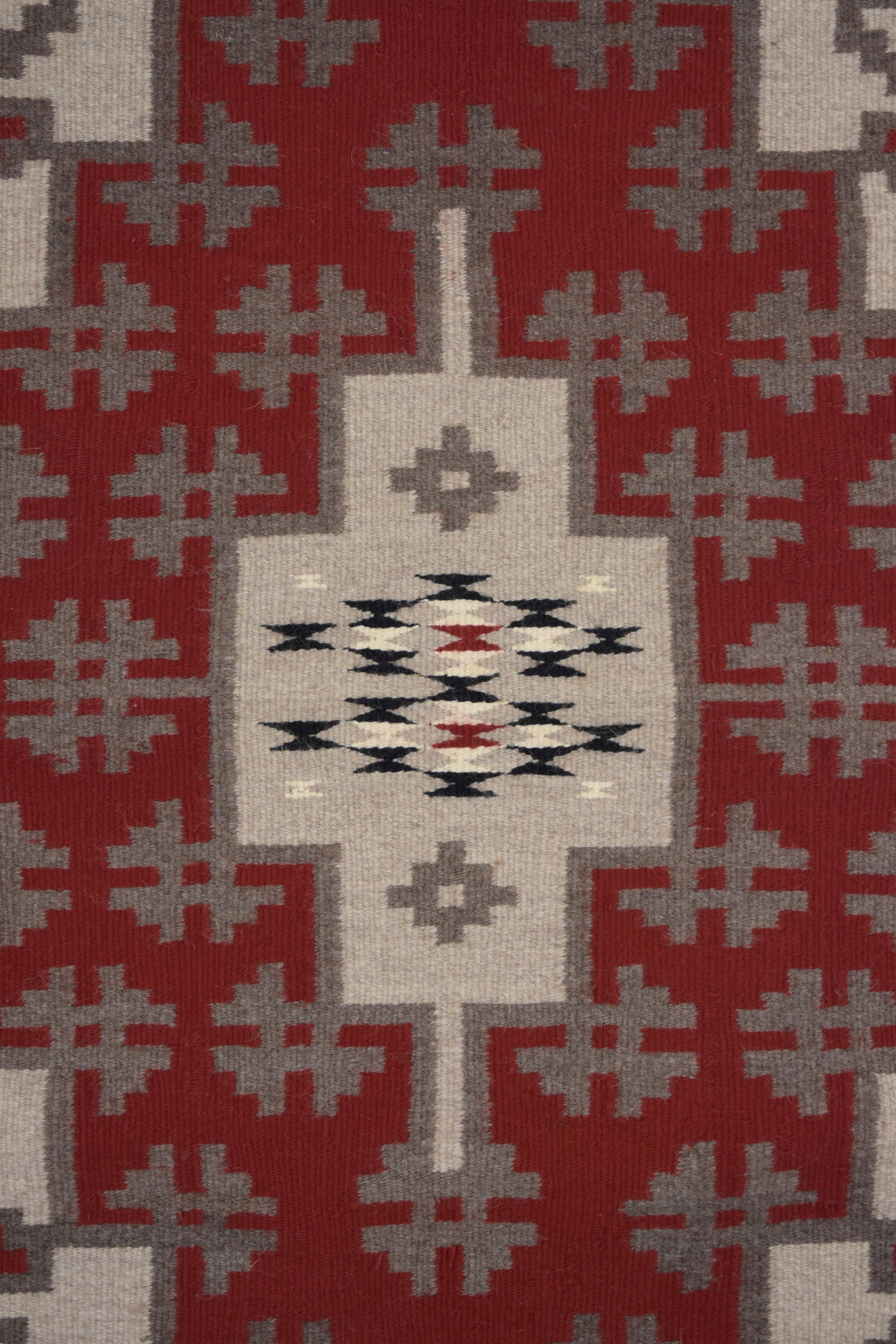 A gorgeous early 20th century Navajo rug with a fantastic pattern containing stepped beige medallion and gray clovers all on a red background. The border is simple with solid black and cream-colored stripes.
  
