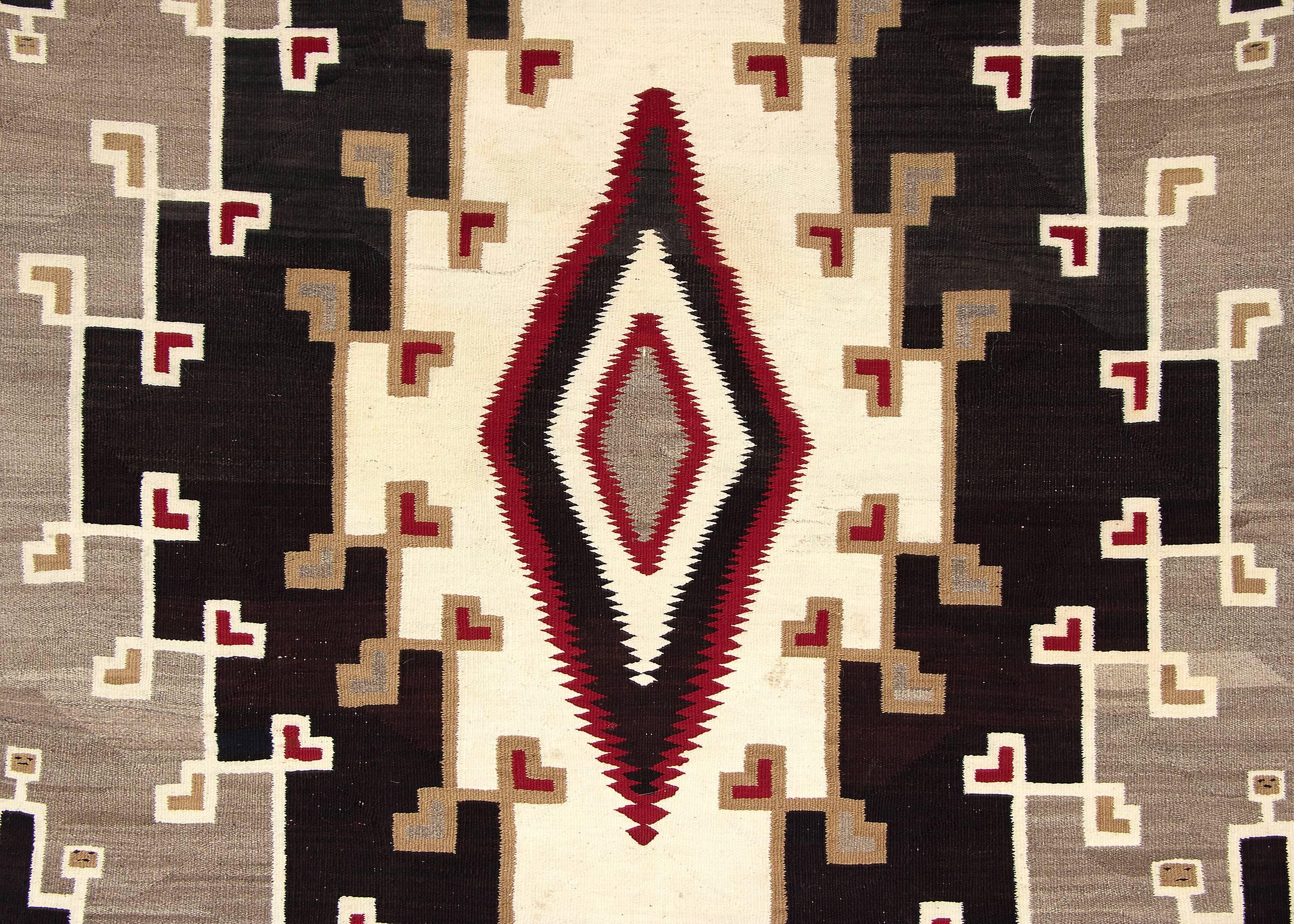 Large Navajo textile from Klagetoh, Arizona, from the early 20th century. Although similar to a Ganado pattern, the palette is more muted with a rare negative background. Unique pictorial faces were woven within the Kiva step designs. 

This