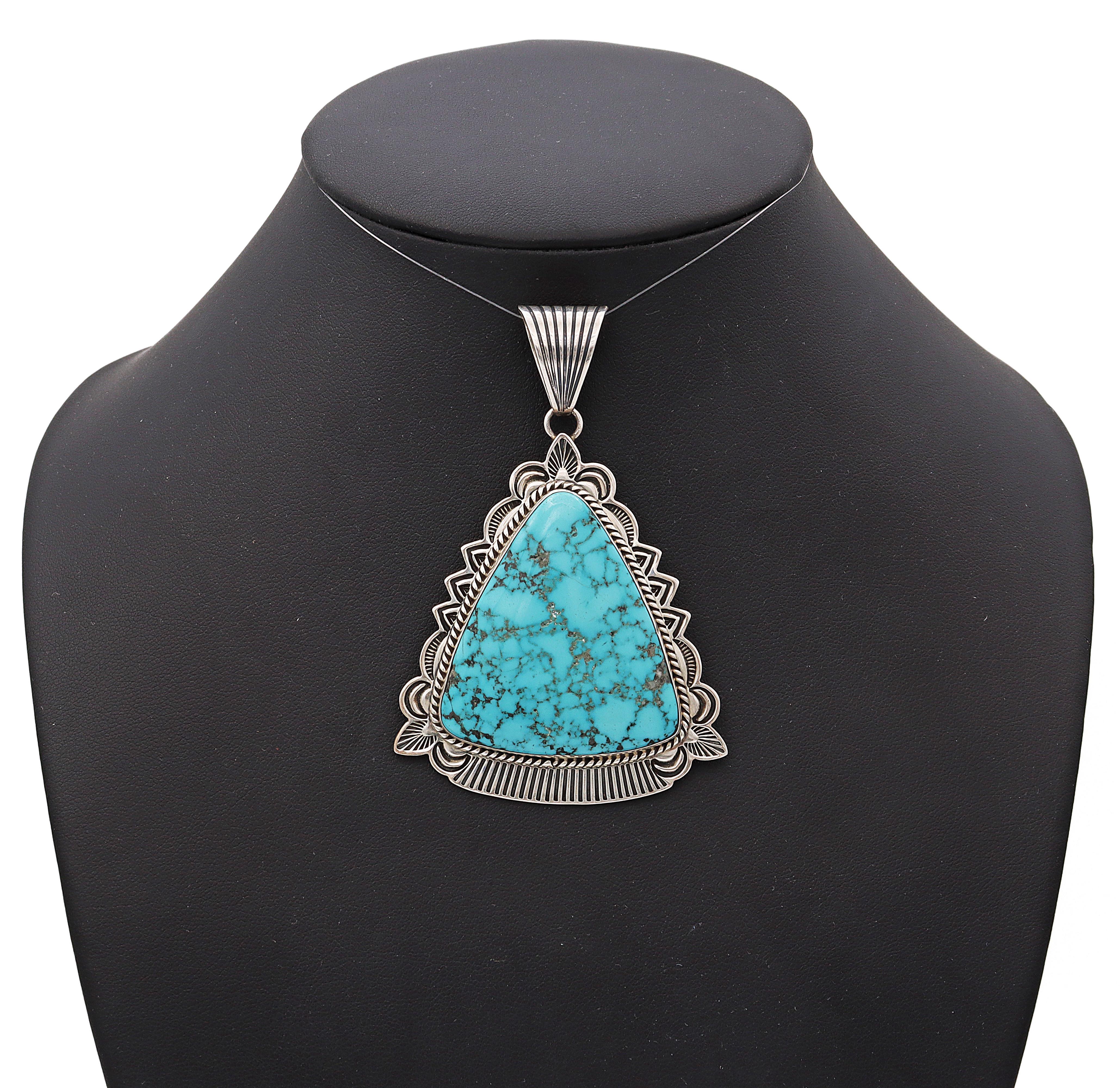 This striking Navajo pendant is a bold expression of Southwestern artistry, featuring a large triangular turquoise stone rich with intricate black matrix veining. Set in a finely crafted sterling silver bezel, the stone is framed by elaborate