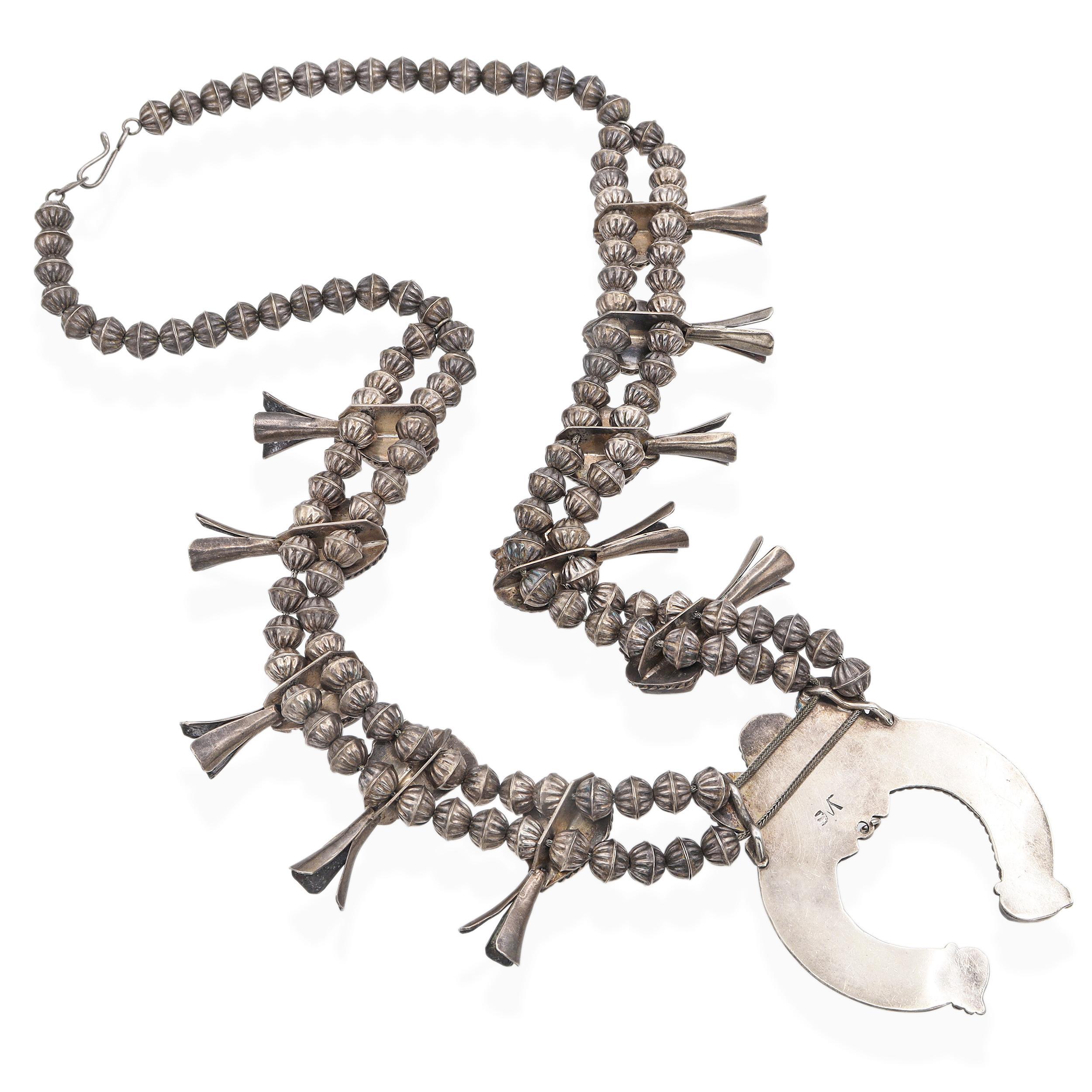 Este collar vintage de flor de calabaza, un sorprendente ejemplo de la artesanía navajo, está elaborado en plata de ley y engastado con piedras de turquesa natural que muestran patrones de matriz únicos y vibrantes tonos azul verdoso. La tradicional