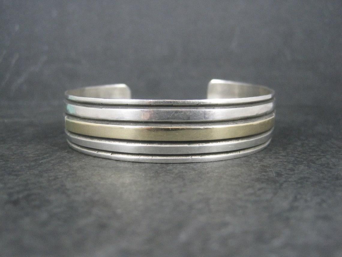 This gorgeous vintage cuff bracelet is a combination of sterling silver and 14k gold.

Measurements: 9/16 of an inch wide - Inner circumference of 6.5 inches including the 1 inch gap
Weight: 25.8 grams

Marks: Sterling, 14K Aron Johnson

Condition: