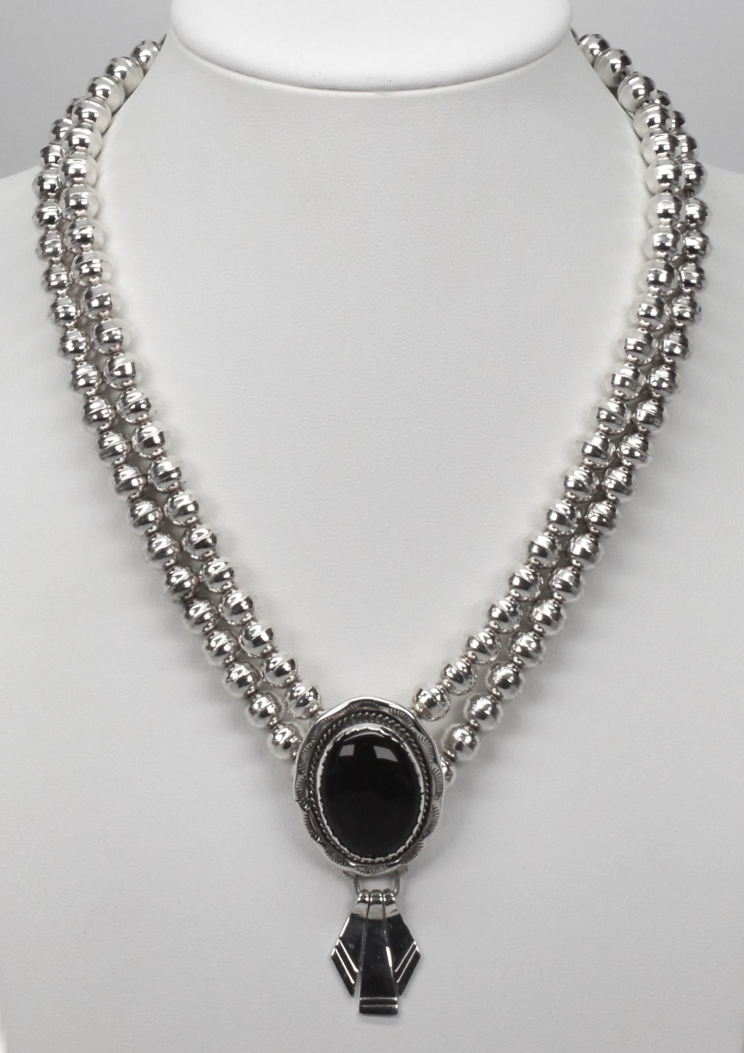 The striking pendant displays a 17 x 23mm black onyx oval cabochon, bezel set in hand-tooled sterling silver that is the feature of this JM Navajo design. Three silver tassels dangle from the 1 x 1 1/4 inch oval pendant which is integrated into a