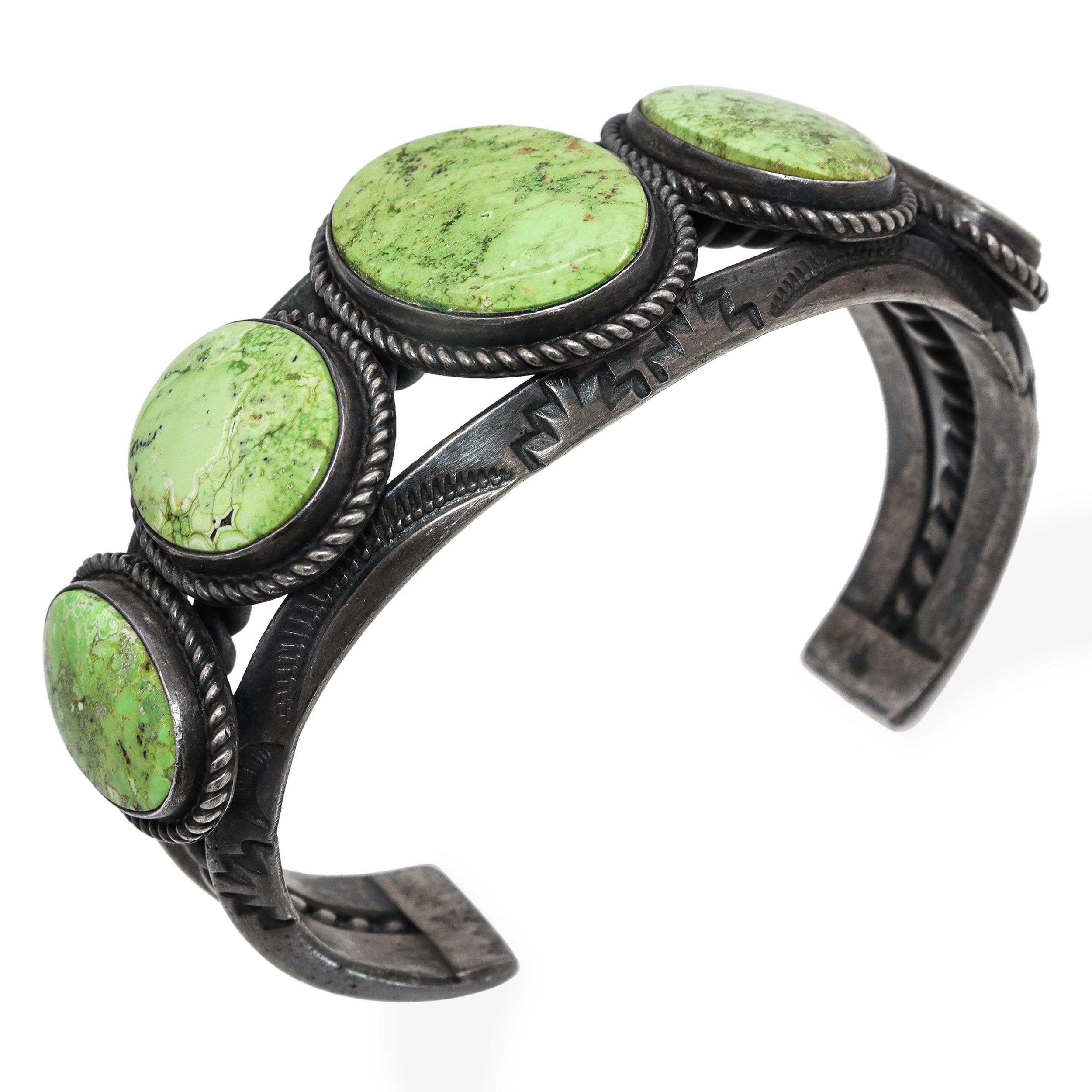Questo audace bracciale vintage Navajo è un esempio di artigianato tradizionale del Sud-Ovest. Il bracciale presenta cinque grandi cabochon ovali di turchese verde, ognuno dei quali mostra variazioni uniche di matrice e ricche sfumature verdi che