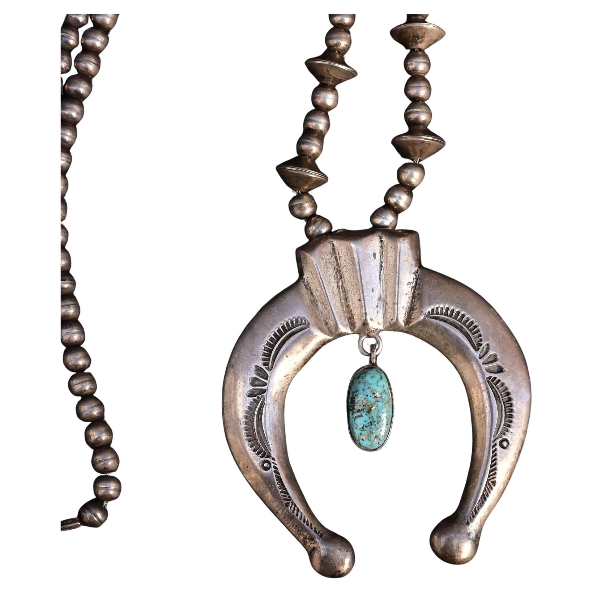 This bold and traditional Navajo necklace features a striking sterling silver Naja pendant accented with hand-stamped details and a natural turquoise cabochon at the center. The necklace measures approximately 13 1/4 inches long and is strung with a