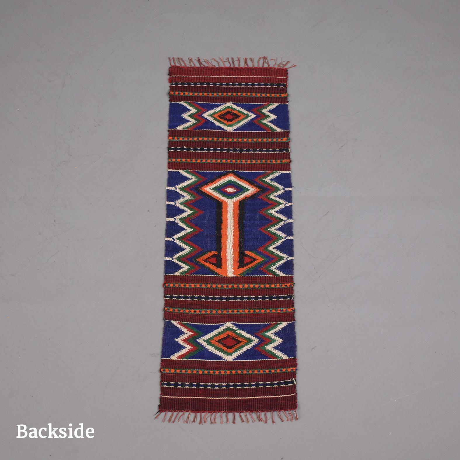 A vintage handwoven Navajo-style rug in good condition. This wool rug features a Native American traditional design pattern of stepped cross-shapes and hooks over a red ground. rendered in a palette of red, blue, white, black, and green.