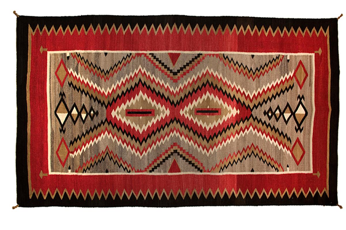 Vintage Southwestern/Navajo rug. Woven of native handspun wool in a geometric stylized diamond pattern in natural fleece colors of gray, ivory/white and brown/black with aniline red. This textile is well suited for use on the floor as an area rug or