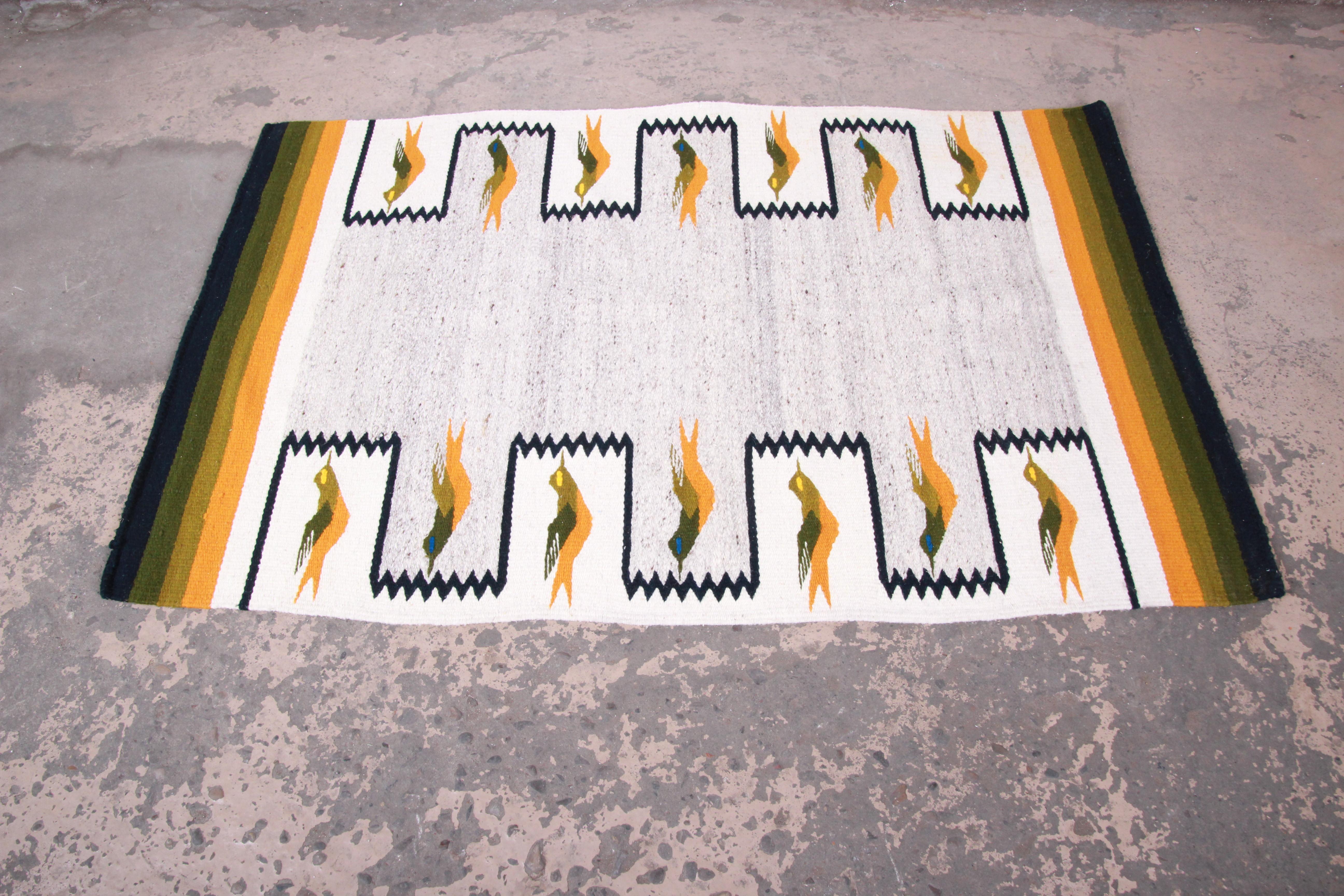A beautiful handwoven vintage Navajo rug or wall hanging. The rug is made from 100% wool and features a unique geometric bird design, with predominant colors in ivory, yellow, green, and navy blue. The rug can be used on the floor but is also ready