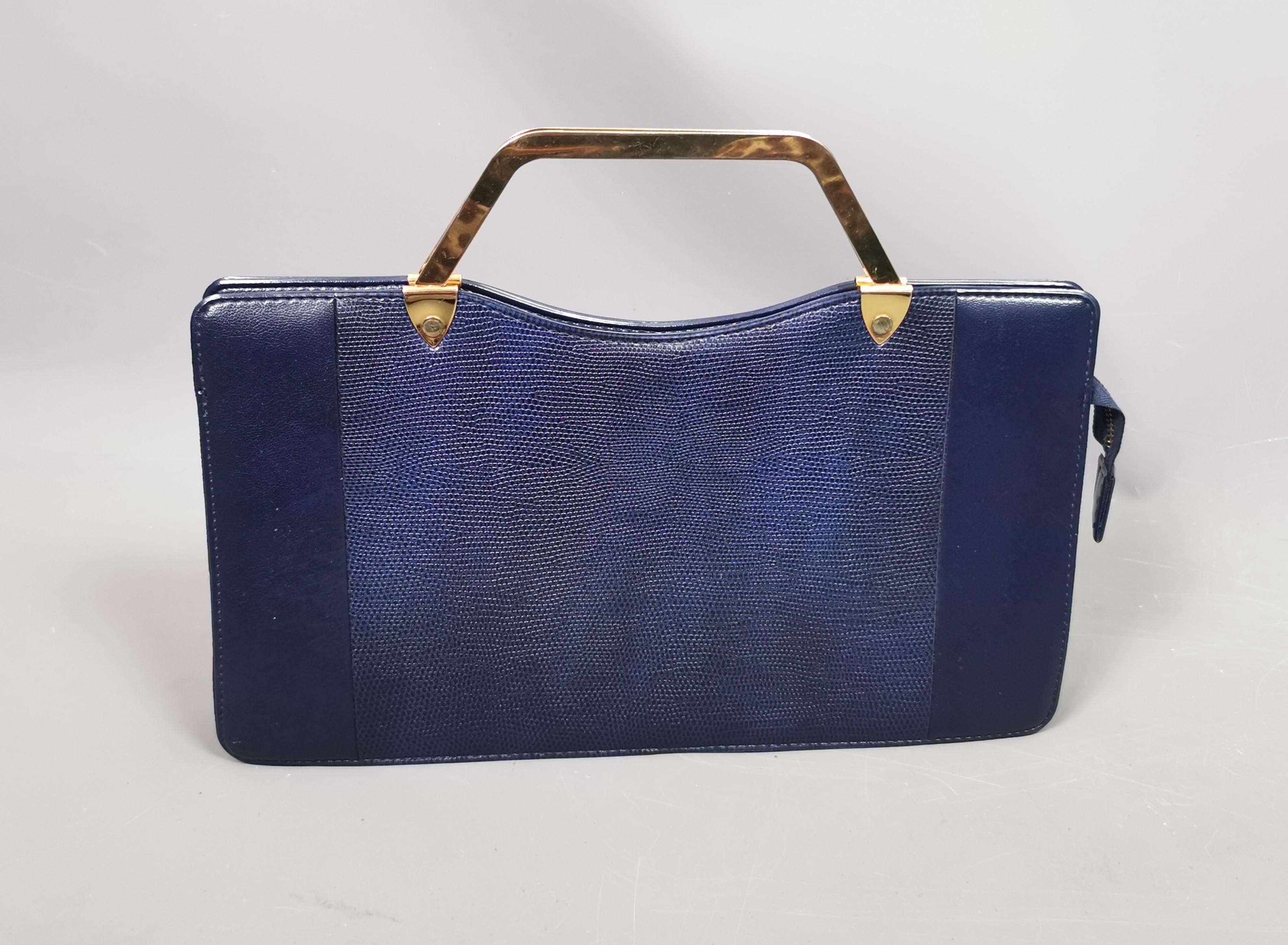 A gorgeous vintage c1980s faux snakeskin handbag.

It is a navy colour leather with a faux snakeskin design to the front and back centre with smooth ends.

The bag has geometric shape gold tone metal top handles and opens with a zip