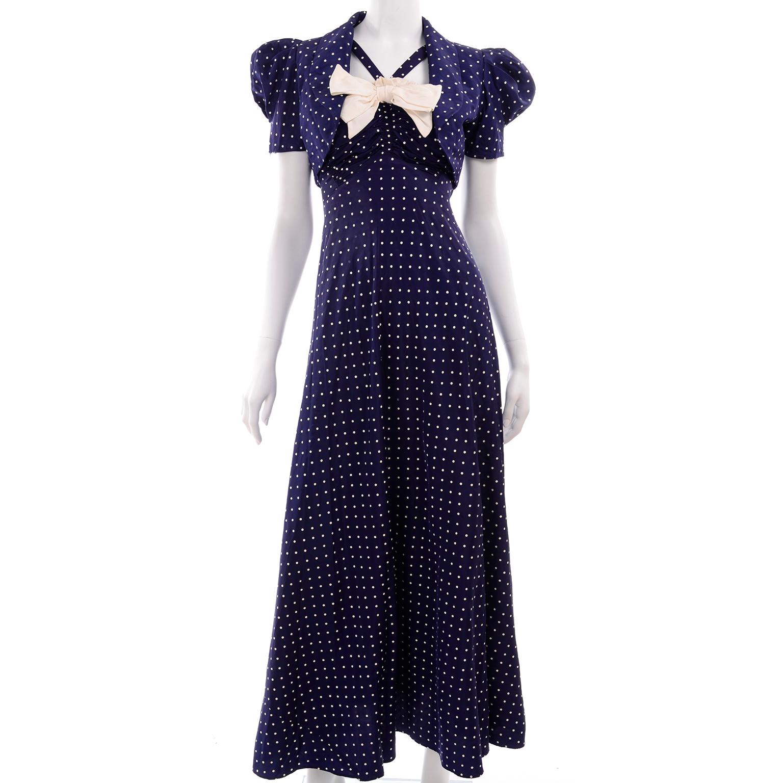 This is an adorable long dark blue vintage dress with tiny white polka dots and a matching cropped bolero jacket, from the late 1930's or early 1940's. The bust of the dress is gathered, with a white ruffle trim that has a large white bow in the