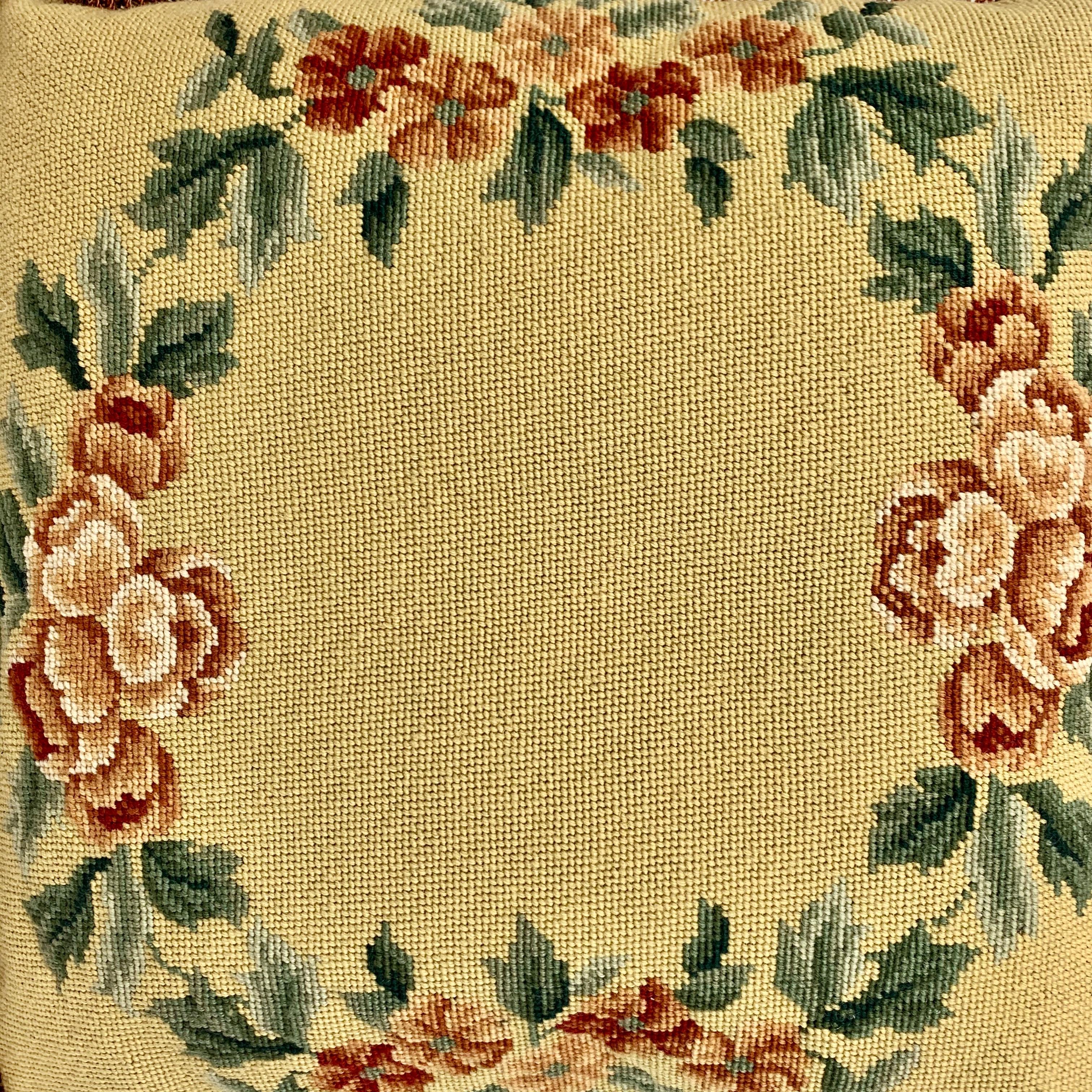 Vintage hand needlepointed cushion or decorative pillow. The design is a garland of tomato red flowers and green leaves on a golden wheat ground. The trim is a coordinating tomato red fringe and the newly added backing is damask in a mellow wheat