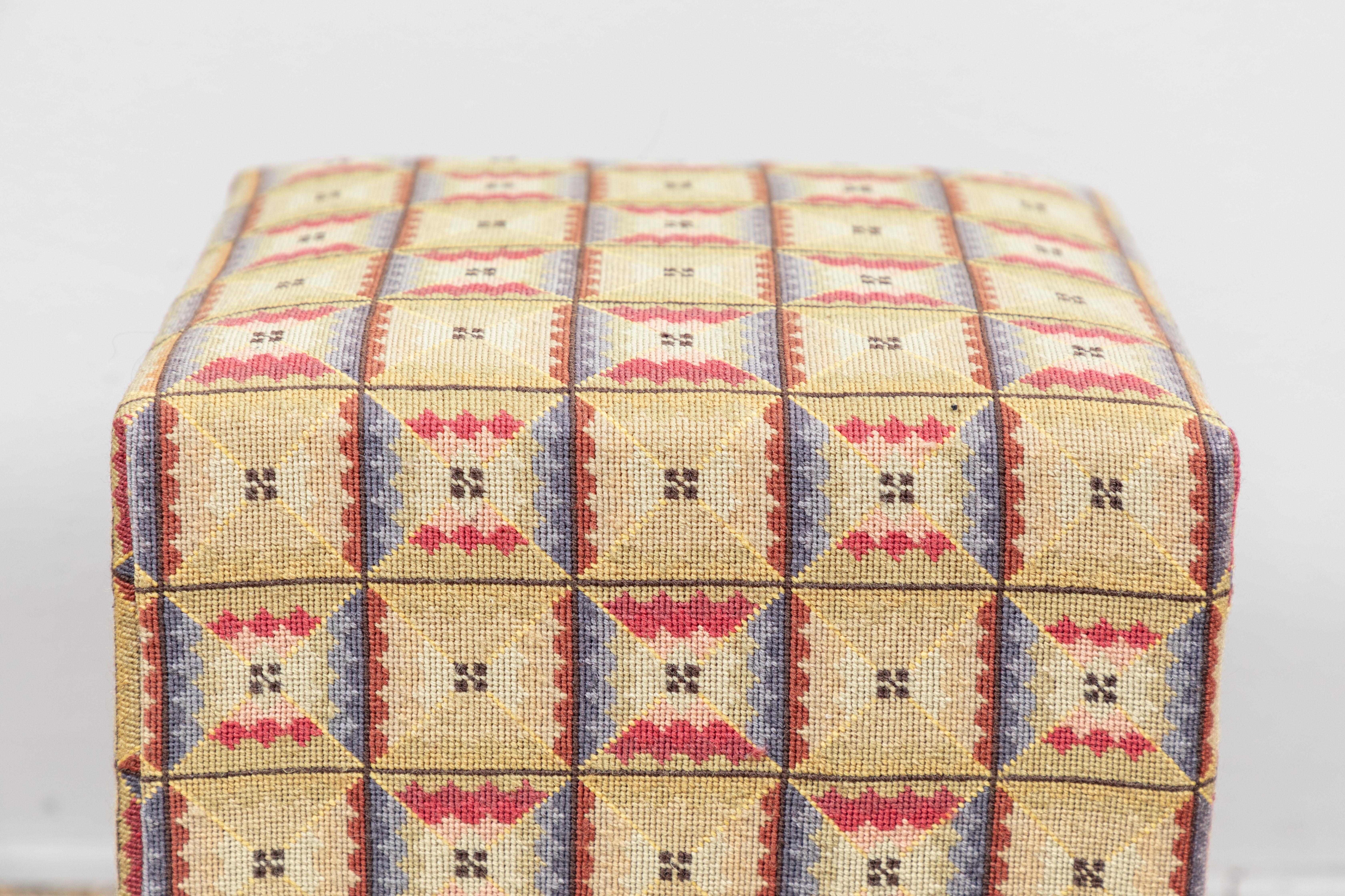 Yellow, blue, ivory and red needlepoint used as upholstery on small footstool.