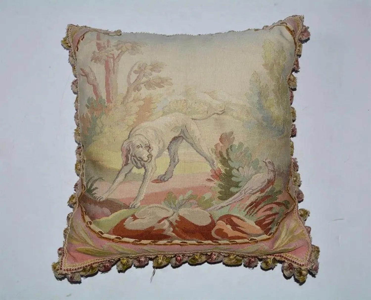 
The front of the vintage pillow is covered in fine multicolored needlepoint depicting a hunting dog and pheasant within a leafy landscape. The back is covered in raspberry cotton velvet. Bullion fringe embellished all four edges. All parts of the