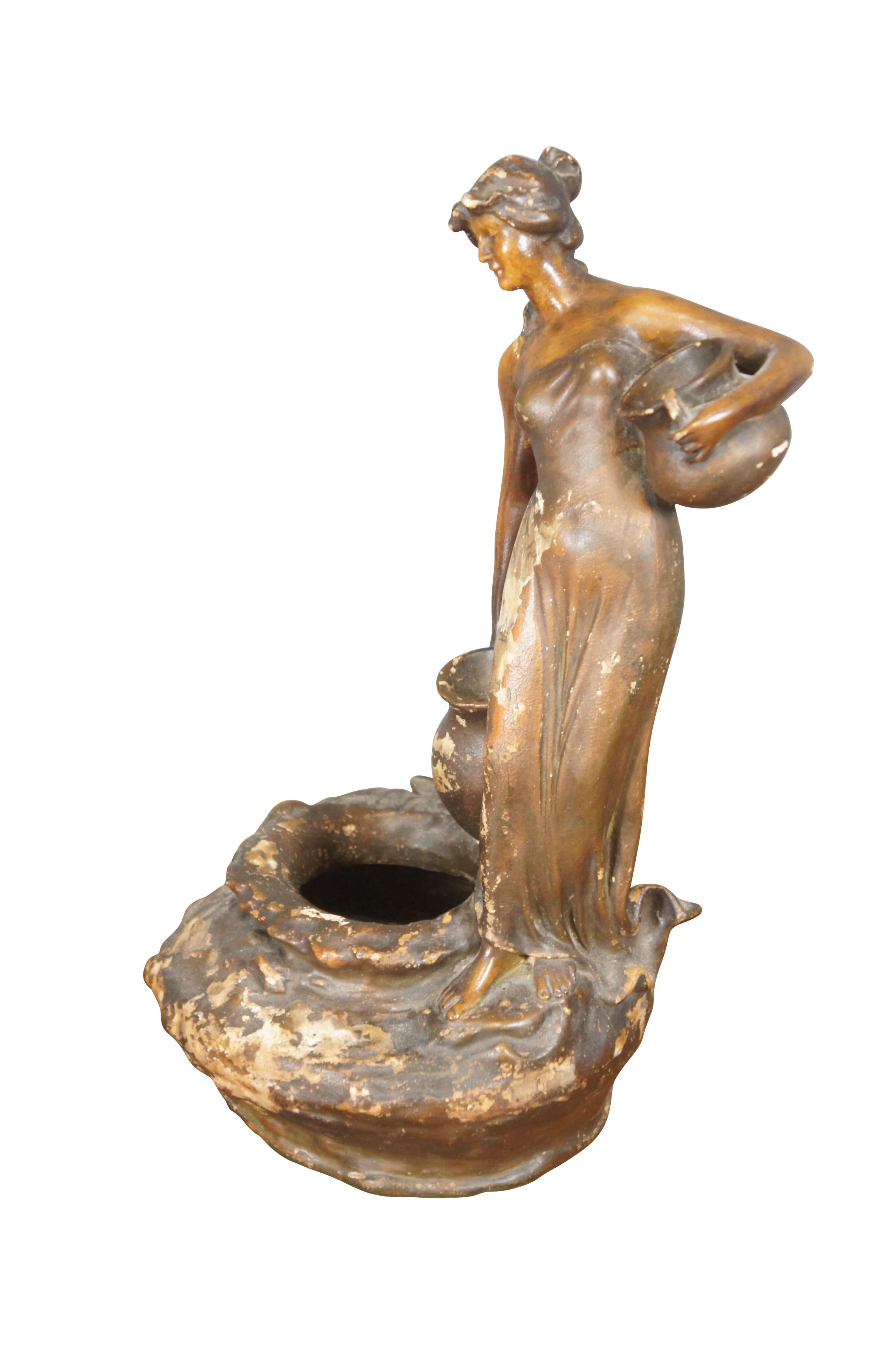 Statuetta / vaso corto in gesso dipinto di marrone della metà o dell'inizio del XX secolo a forma di donna alta in stile neoclassico / art nouveau che trasporta brocche d'acqua sul bordo di un pozzo.

Dimensioni:
10