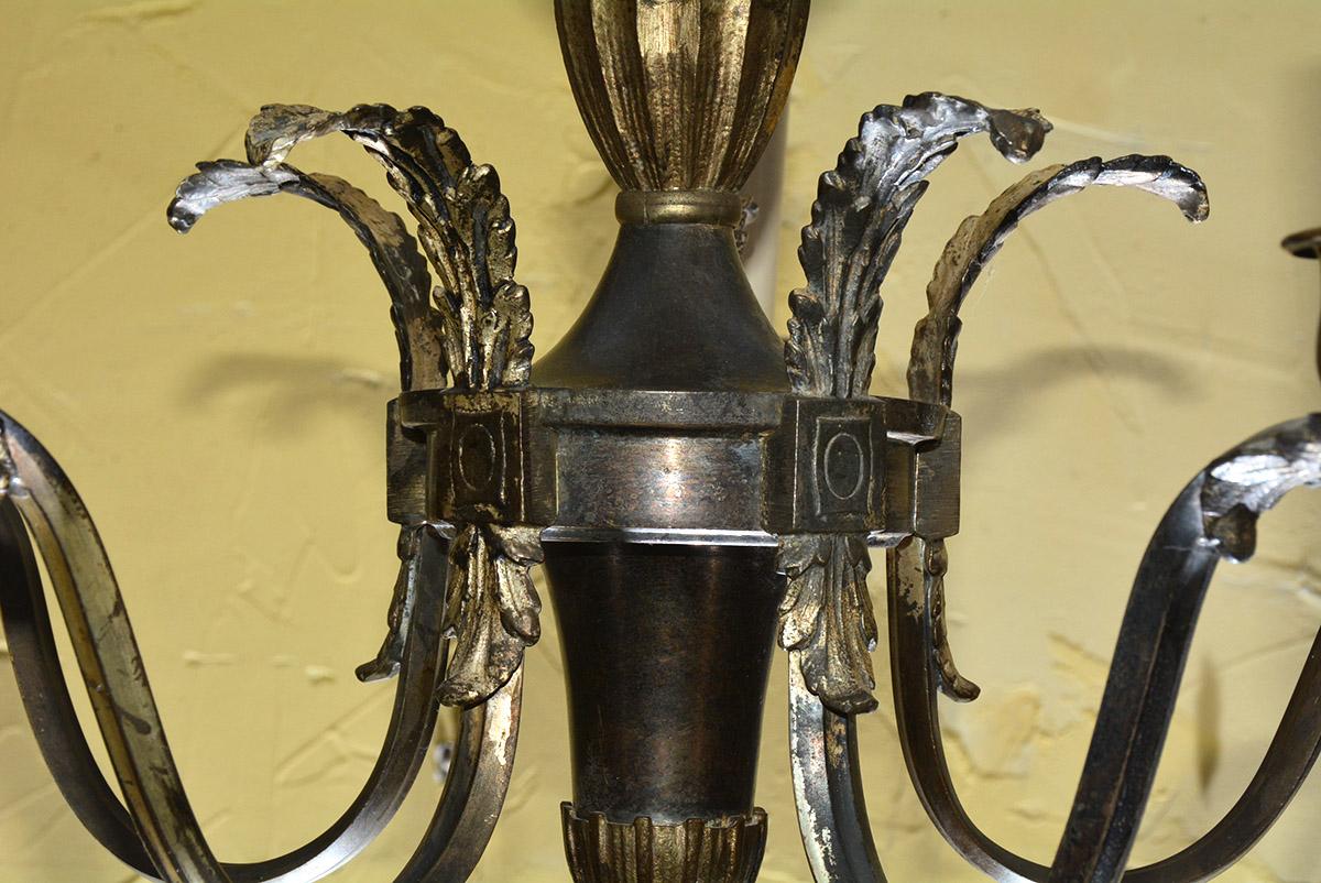 Der kleine, aber sehr präsente Vintage-Kronleuchter aus gold- und bronzefarbenem Metall weist die Merkmale des neoklassischen Stils auf: fünf blattförmige Armaturen, die an einer zentralen Urne befestigt sind, die von einer Krone gekrönt wird und