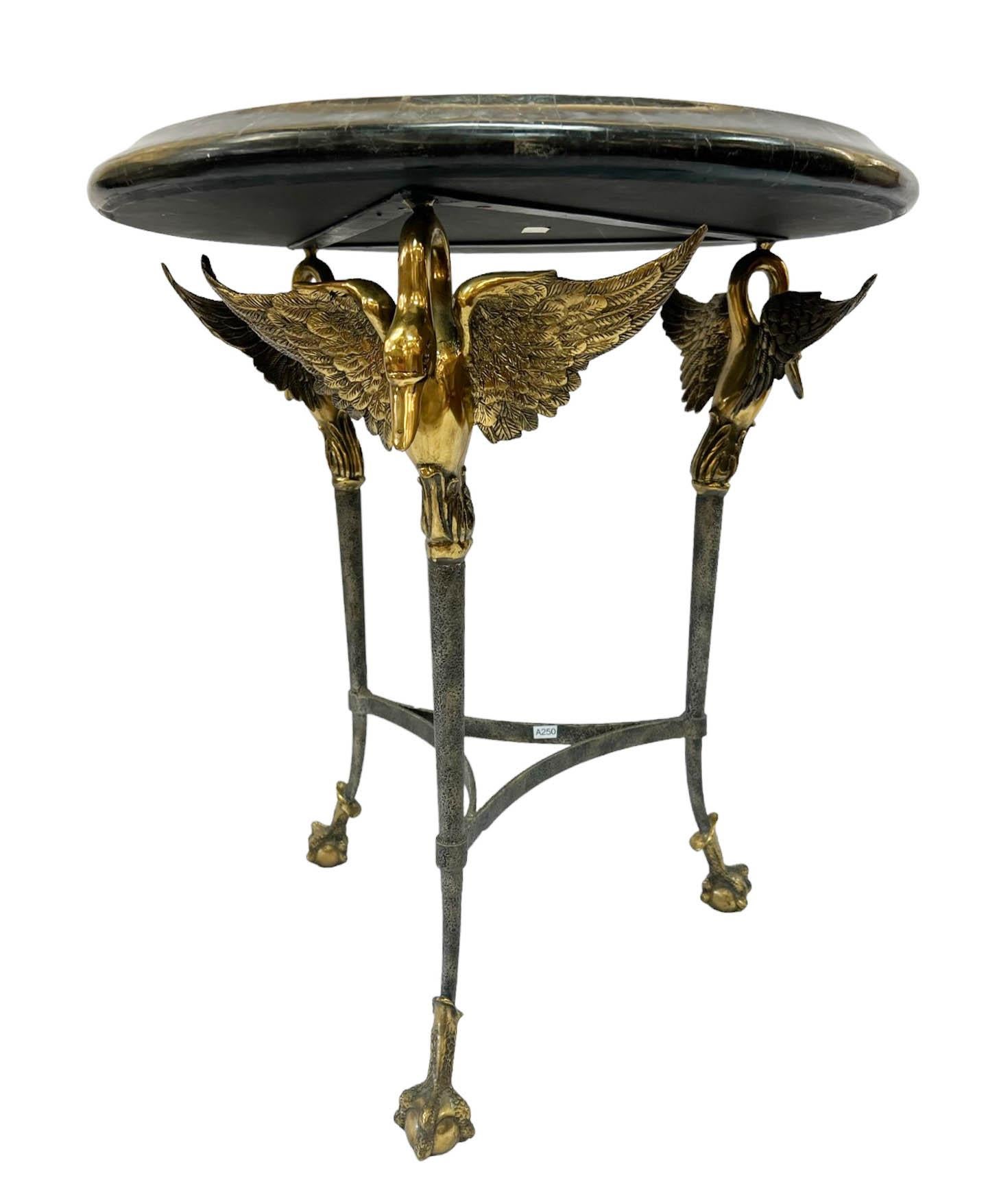 Magnifique table d'appoint de style néoclassique par Maitland Smith. La table présente un plateau en marqueterie de marbre soutenu par trois pieds en forme de cygne. Un magnifique cygne en laiton aux ailes ouvertes couronne chaque pied de table.