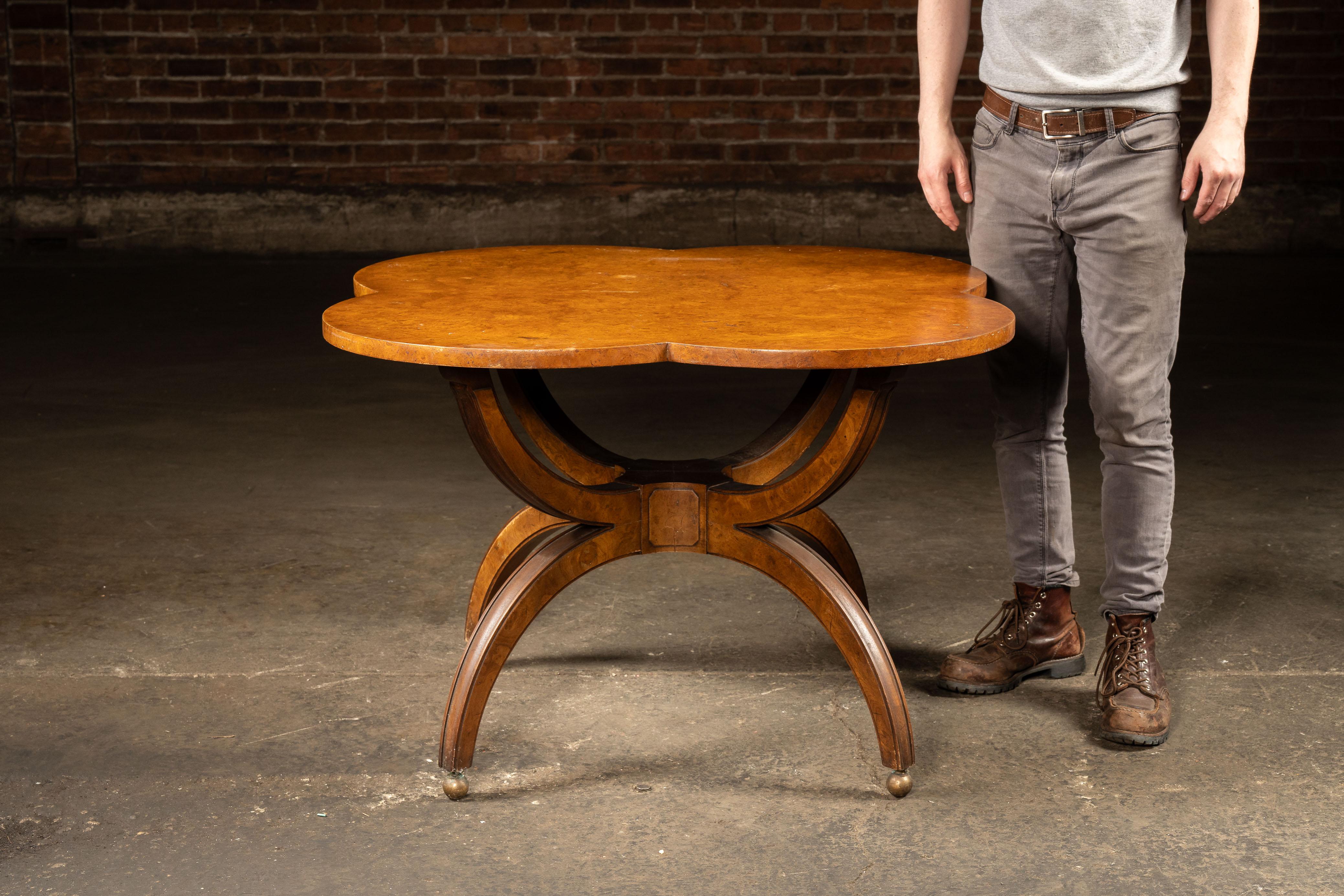 Burled maple table on curved saber legs.

Featuring a clover-shaped top in richly figured burled maple veneer, this mid-century center table balances decorative flair with architectural symmetry. The sculptural saber legs curve outward from a
