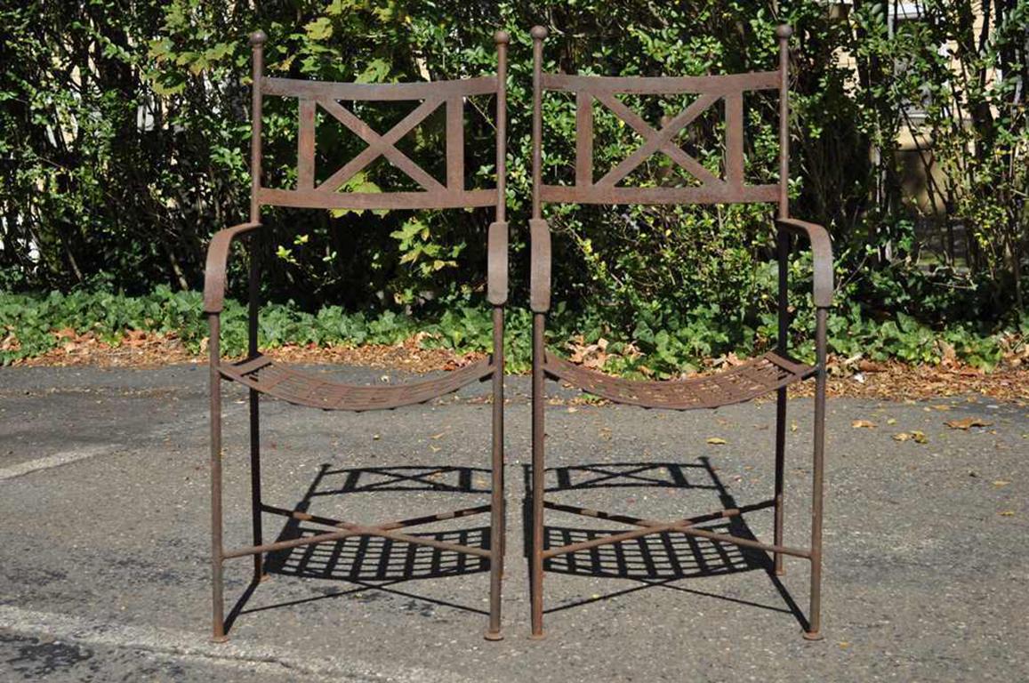 Pair of remarkable Regency / neoclassical style vintage heavy iron garden armchairs. The chairs feature a very sturdy construction with X-form stretcher supported legs, riveted slat seats, and a highly desirable rusted and weathered overall finish,