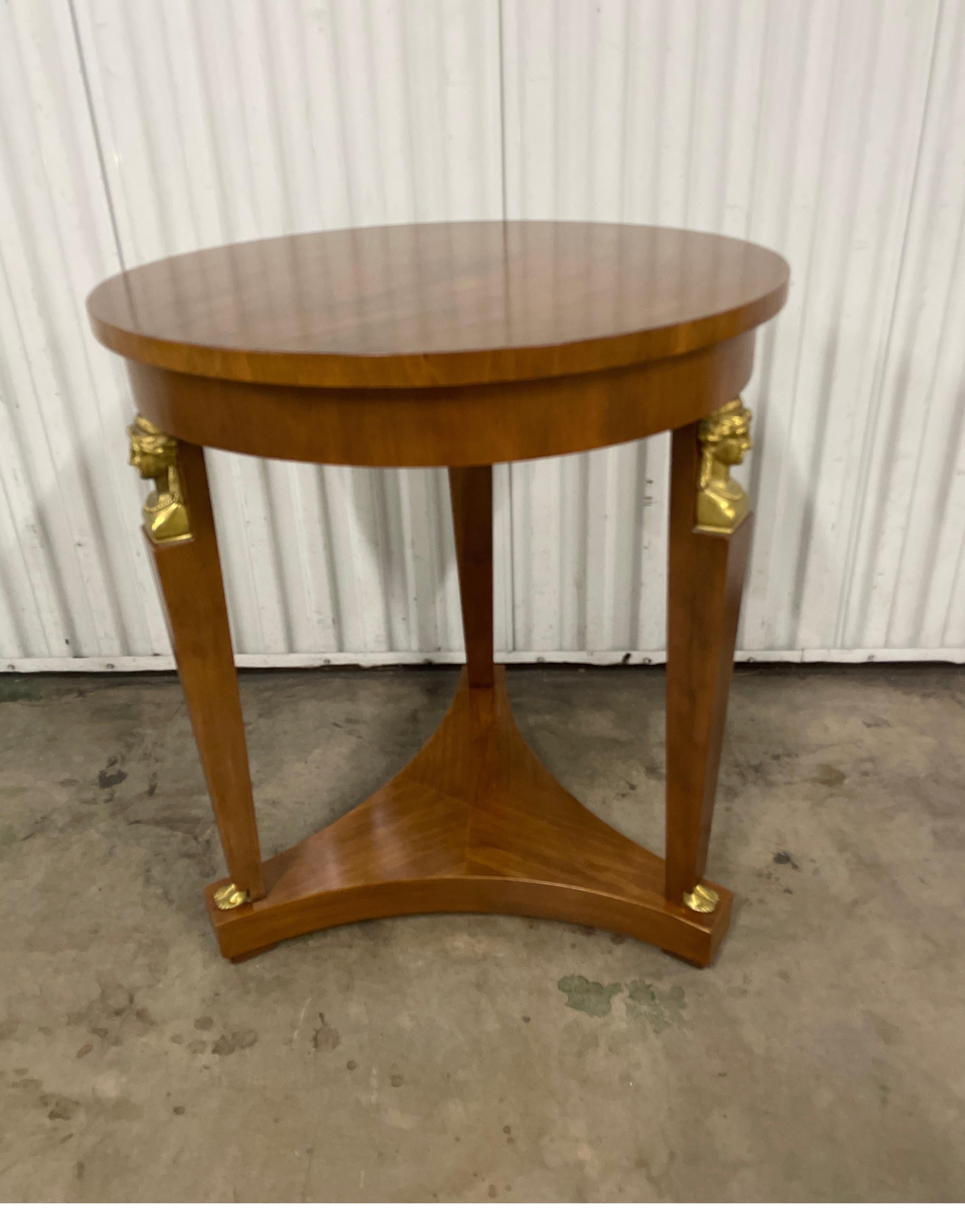Vintage Neoclassical style round side table by Baker Furniture Company. This striking table has three legs attached with a bottom apron. Each leg has a brass face of sphinx at top and finished with a brass foot at base. A very classical and elegant