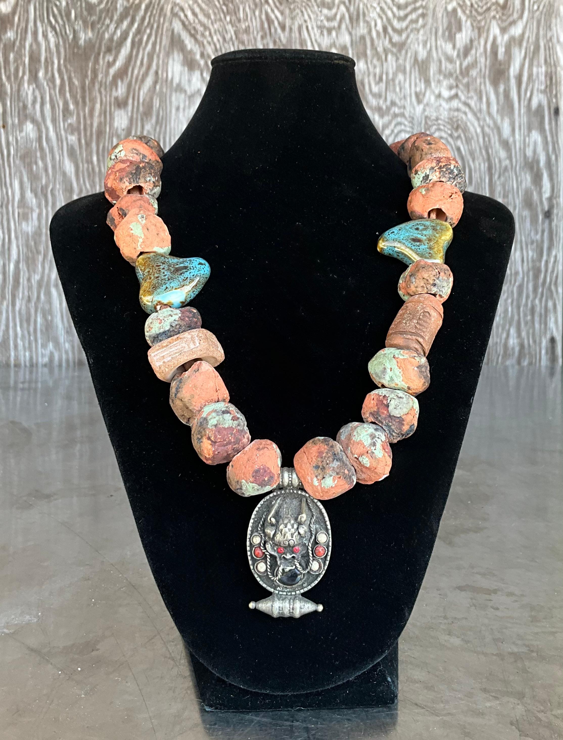 Questa collana vintage in terracotta nepalese con ciondolo tibetano è un pezzo sorprendente che incarna la ricca cultura artistica della regione himalayana. Realizzate a mano con argilla naturale di terracotta, ogni perlina presenta toni terrosi e