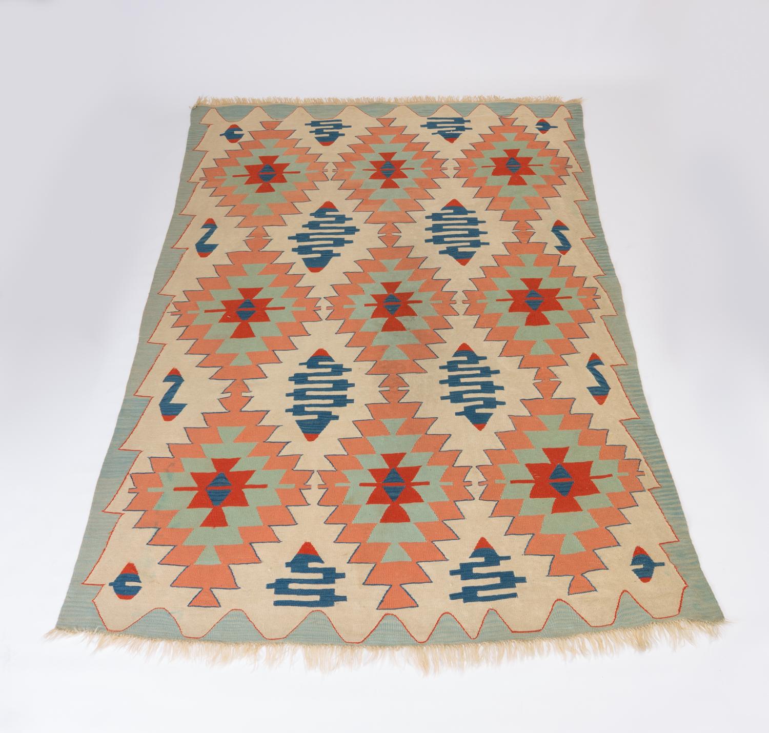 A large Turkish Kilim rug in a muted color palette on a soft, ivory field. This rug is woven with protective motifs in salmon pink, sky blue, terra cotta, and aquamarine hues. 

Condition: Good vintage condition; professionally cleaned. Some