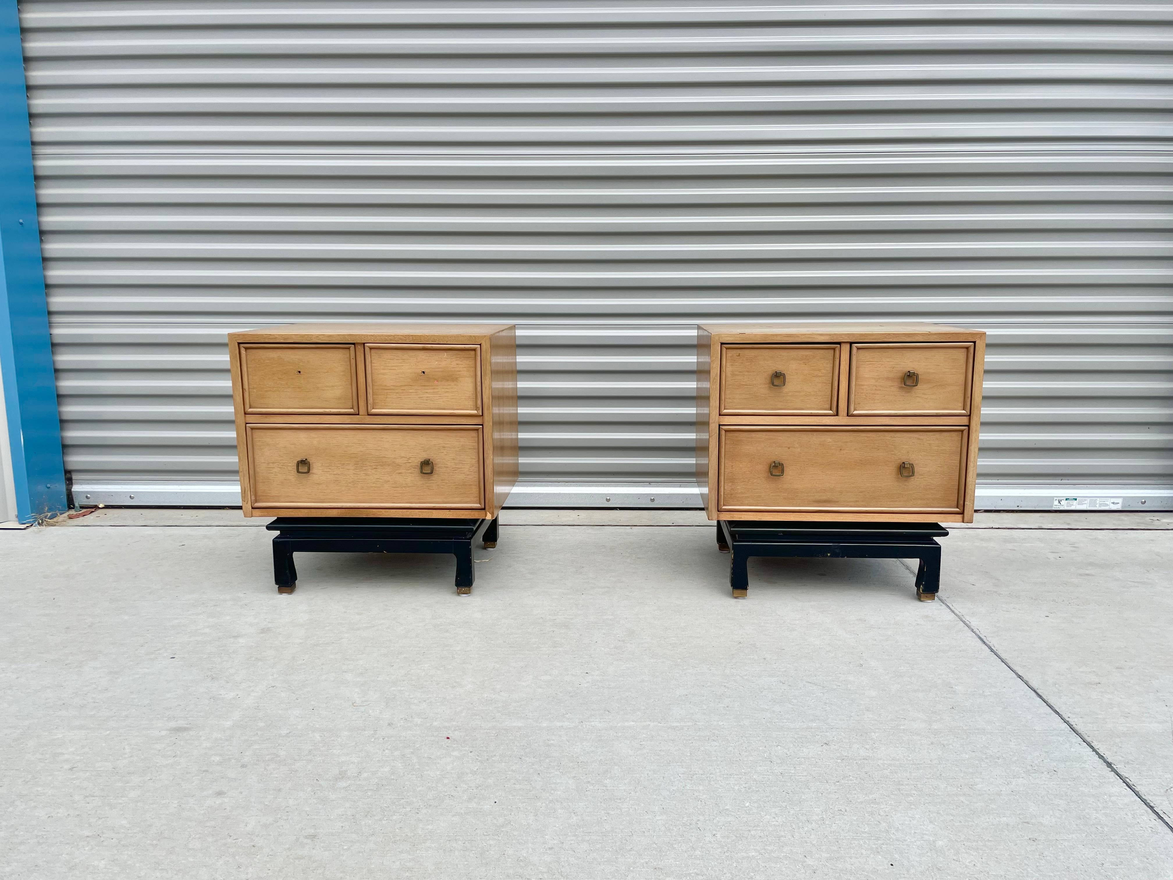 Pair of beautiful nightstands designed and manufactured by American of Martinsville in the United States, circa 1950s. Each nightstand features three dovetailed drawers with original brass pulls and sits on a sculpted black base with brass sabots.