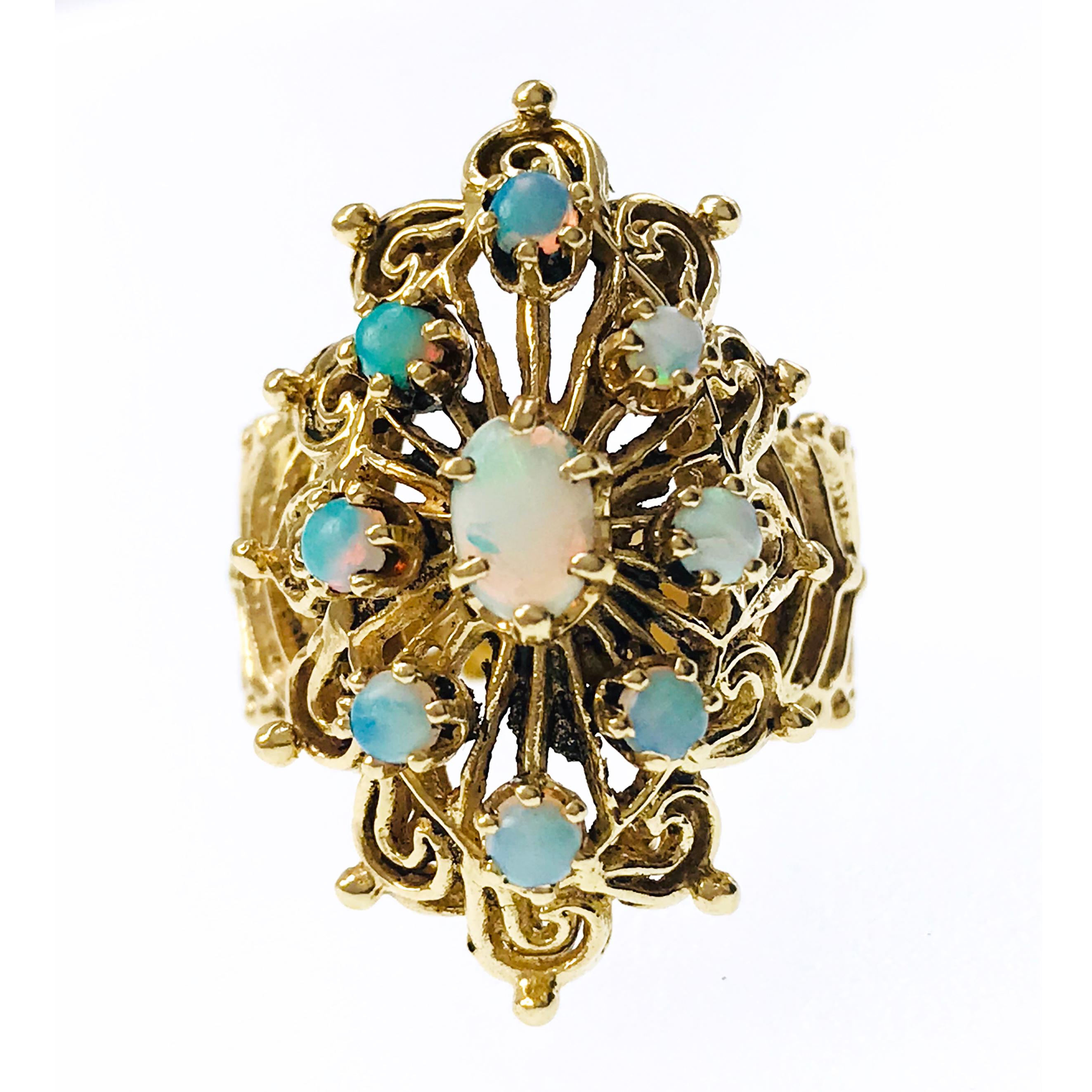 14 Karat Vintage Nine Opal Ornate Ring. One oval six-prong set 6x4mm Opal, with a approximate weight of 0.32ct serves as the central focal point of this scroll designed ring. Eight Opals measuring 2.5mm set in six-prong settings with a total weight