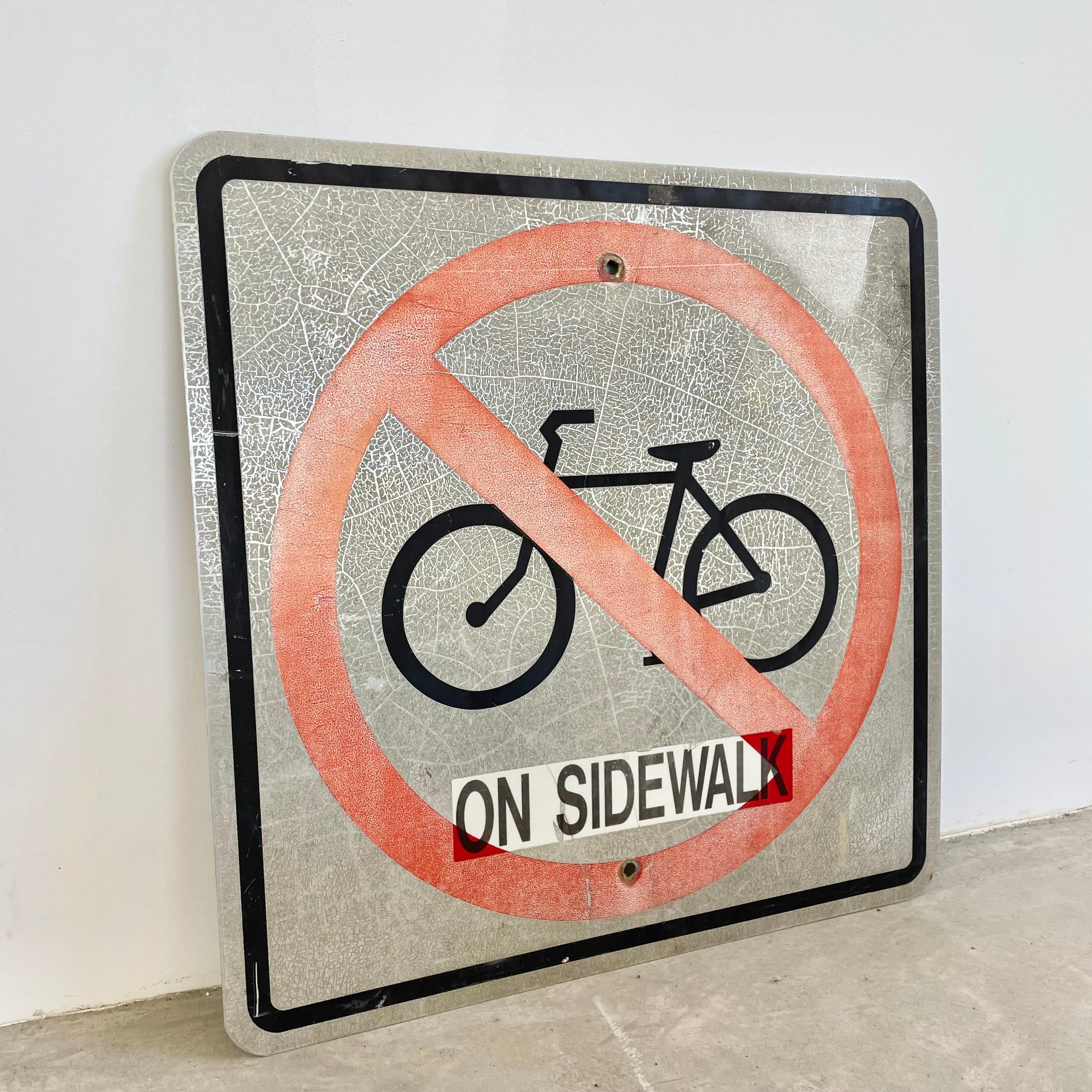 Vintage 'no bikes on sidewalk' sign with incredible sunburn weathering patina. Steel sign featuring a bicycle encircled by a red ring with a line through it. Great faded coloring give this piece unique character. Cool vintage graphics. Perfect for a