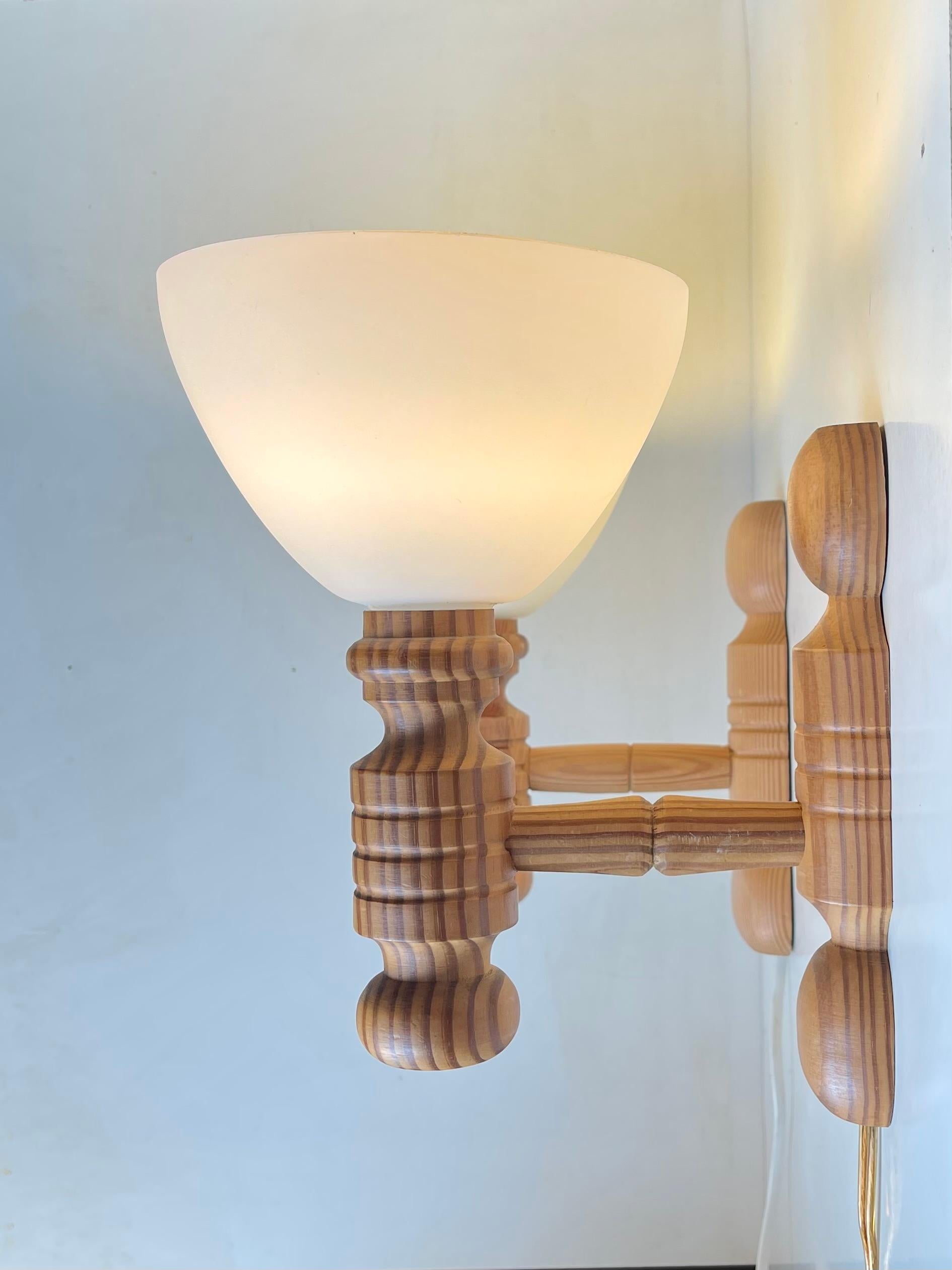 A set of 3 wall lamps fashioned from turned Oregon pine and set with matching shades in white glass. Unknown Scandinavian maker/designer circa 1970-80 in a style reminiscent of Hans Agne Jakobsson and Lisa Pape Johansson. Measurements: H: 26 cm,