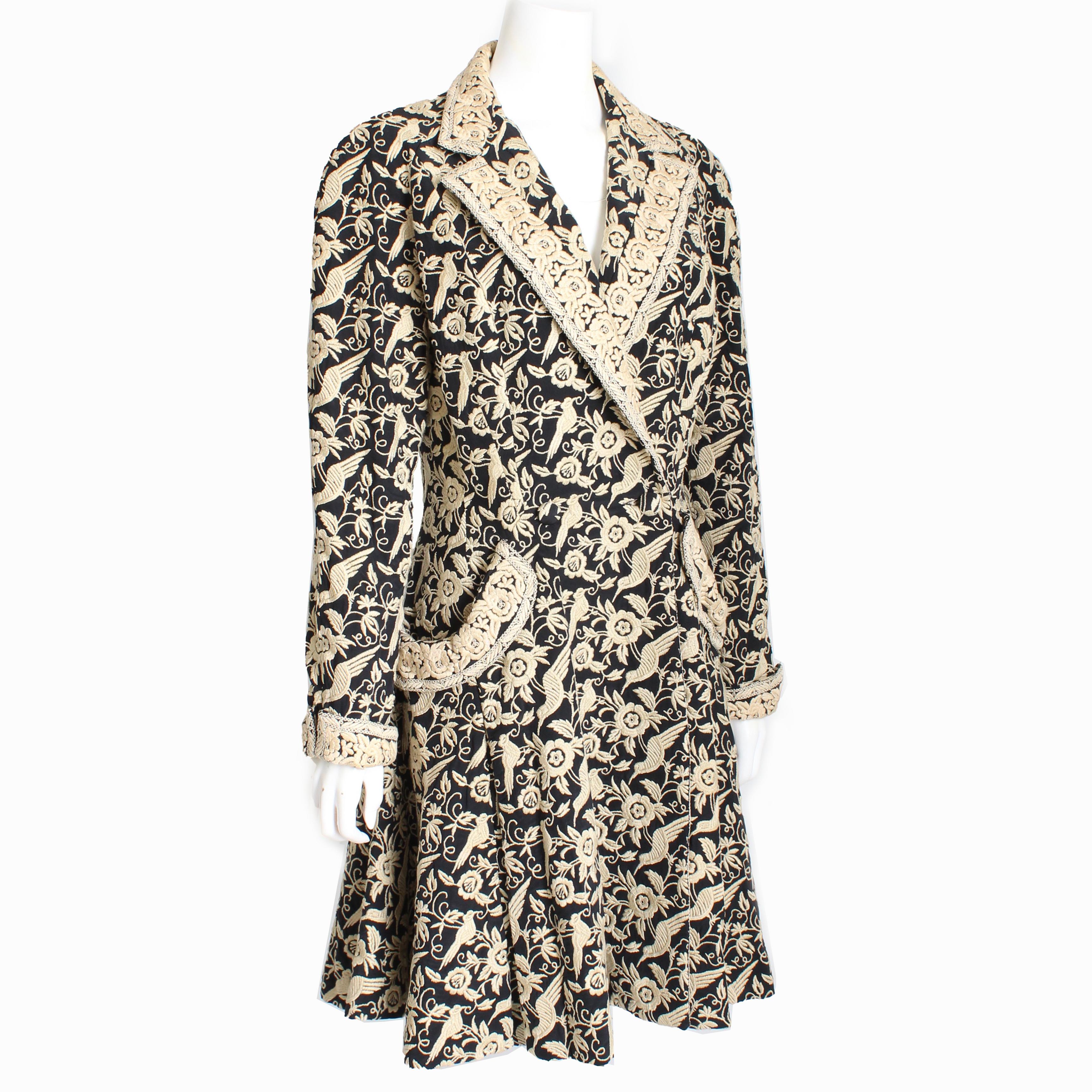 Preowned, vintage Norma Kamali princess-style coat, likely made in the early 90s.  Made from black silk, it features an embroidered pattern of birds and florals throughout, with
cuffed sleeves and oversized pockets.  It fastens at the waist with two