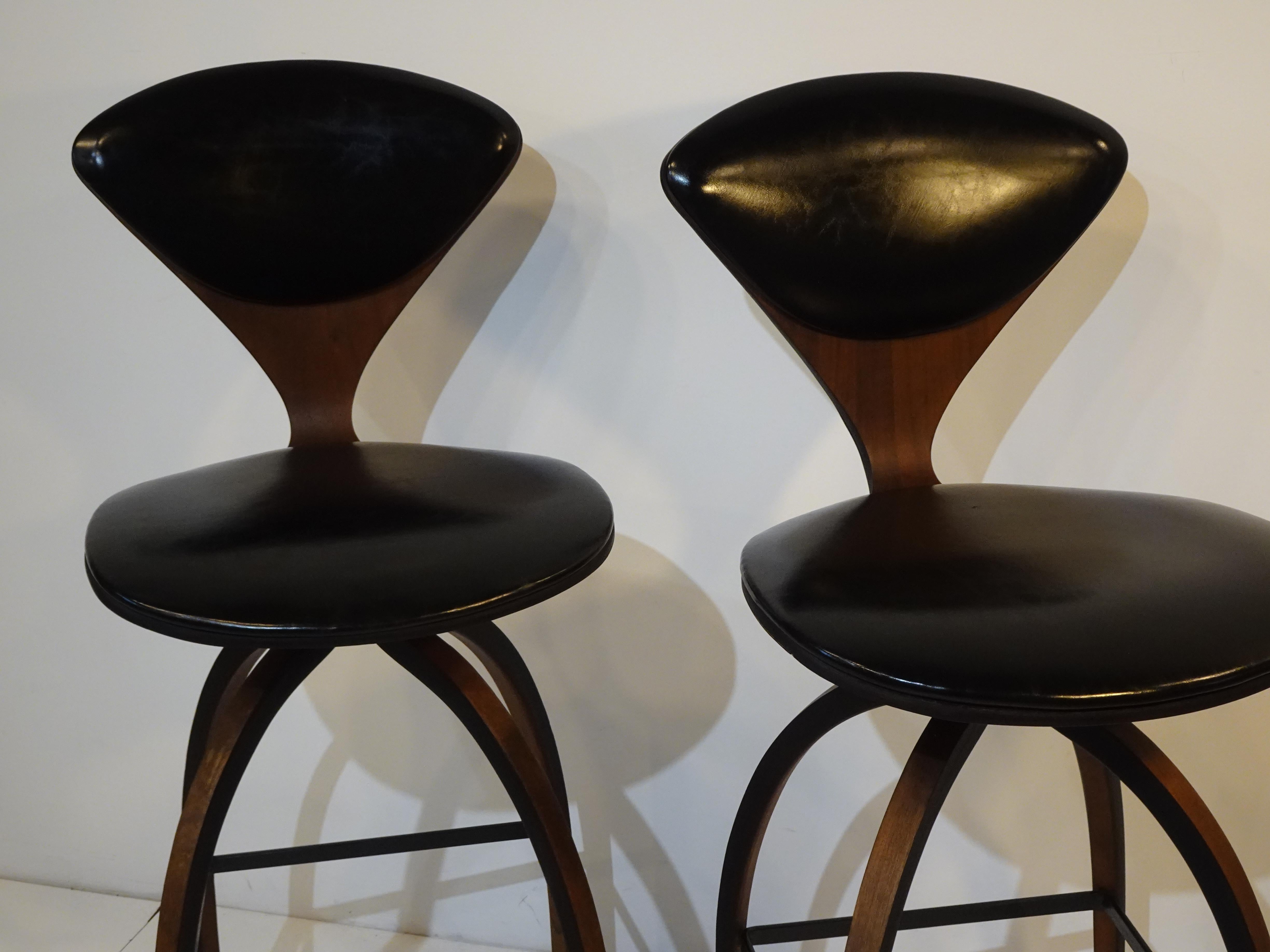 A pair of rare swiveling sculptural molded dark walnut bar stools with black leatherette upholstery on the seat back and bottom. A sculptural look with black metal foot rests and detailed black edge outline to the form designed by Norman Cherner for