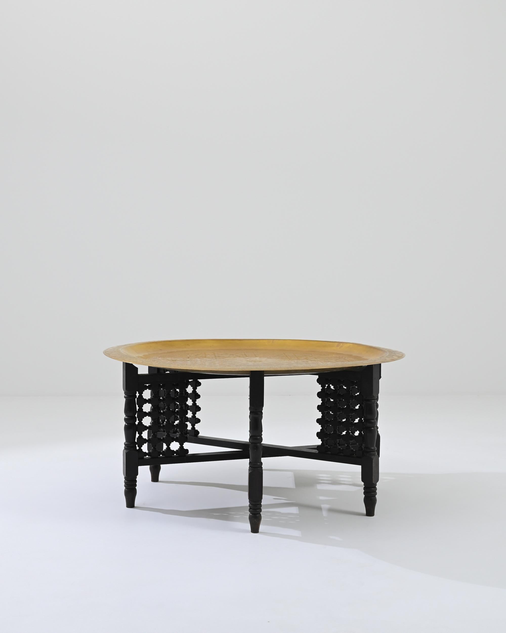 A bray tray tea table on a folding base sourced in North Africa. This spectacular coffee table is a picture of hand-crafted beauty, featuring lathed legs, chiseled patterns, and fastidiously inscribed patterning into its metal top. The combination