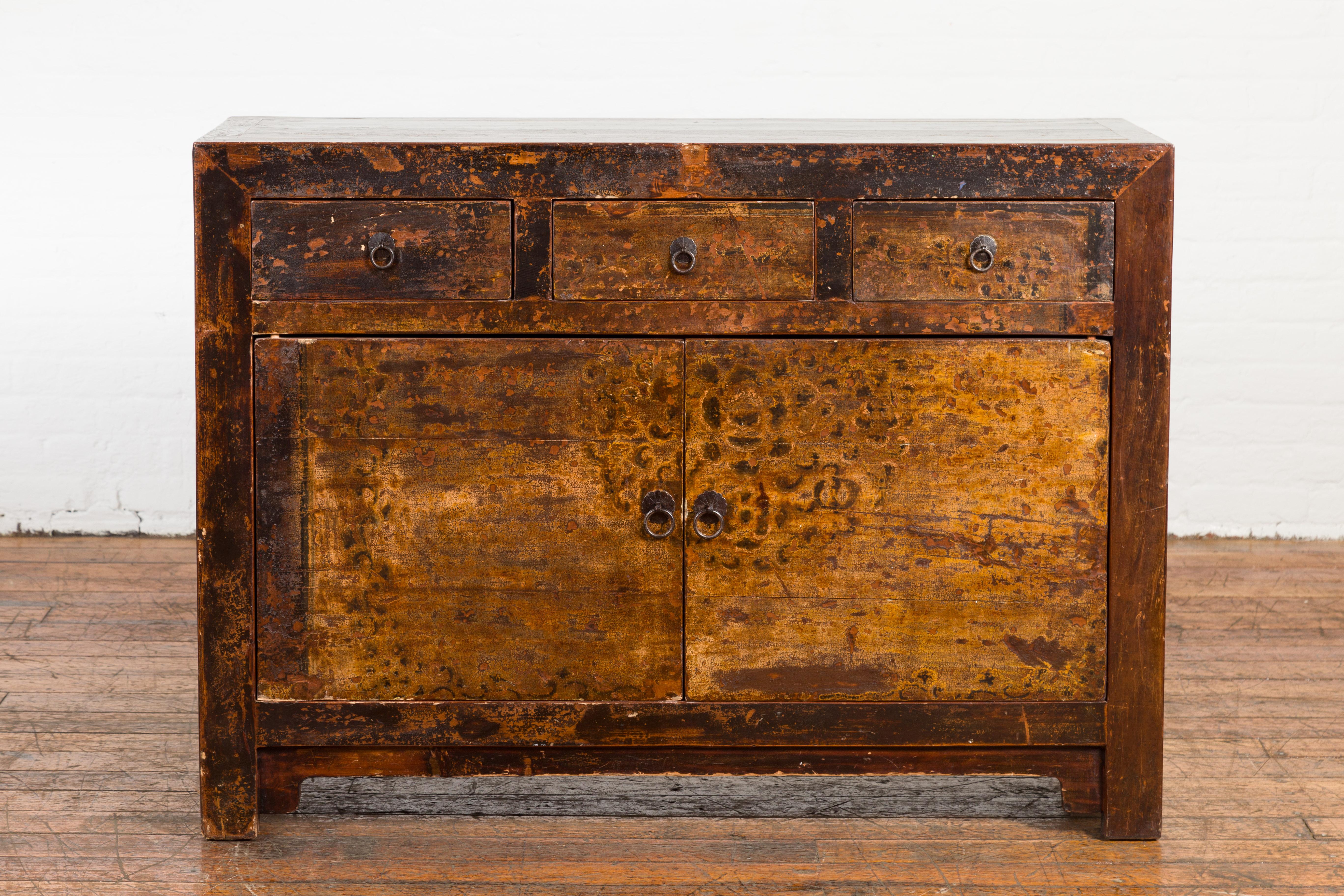 A Vintage Northern Chinese sideboard cabinet from the Mid-20th Century, with distressed appearance and three drawers over two doors. Created in Northern China or Mongolia during the Midcentury period, this sideboard captures the attention with its