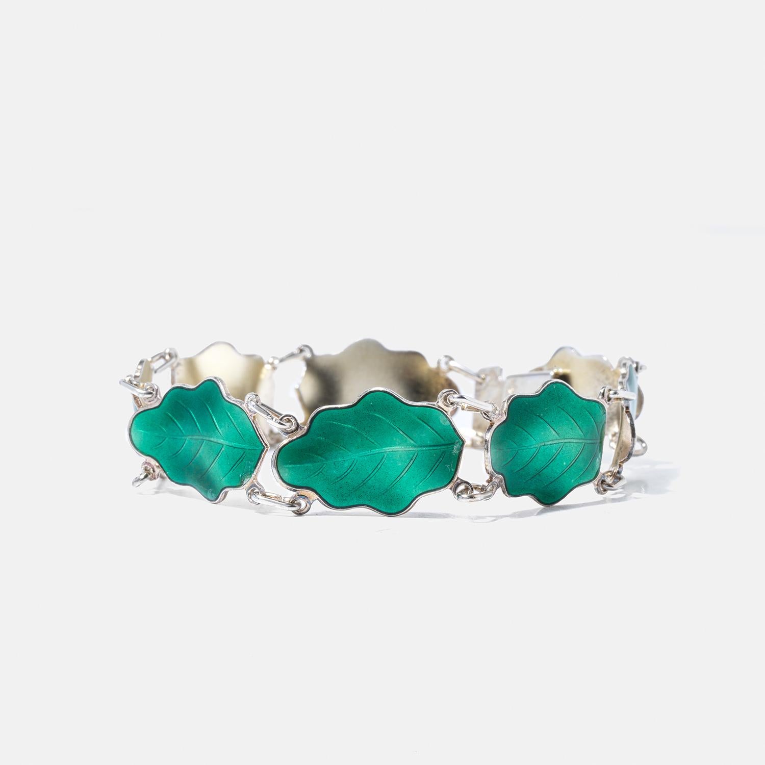 This bracelet is crafted with a series of leaf-shaped links, each featuring detailed, realistic engravings that mimic the intricate veins and contours of leaves. The leaves are made from vibrant green enamel set in polished sterling silver,