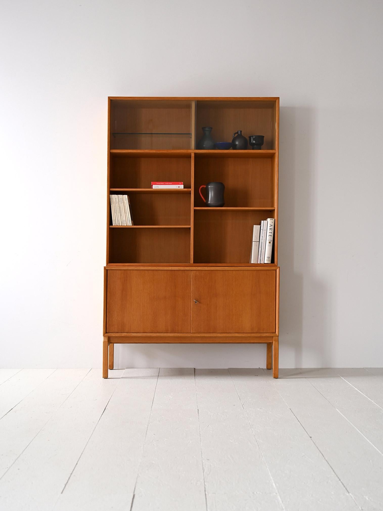 Scandinavian furniture from the 1960s consisting of two modules.

This Scandinavian modernist bookcase is distinguished by its modern lines and the light, golden shade of oak wood.
The lower part is a sideboard with hinged doors on which rests a