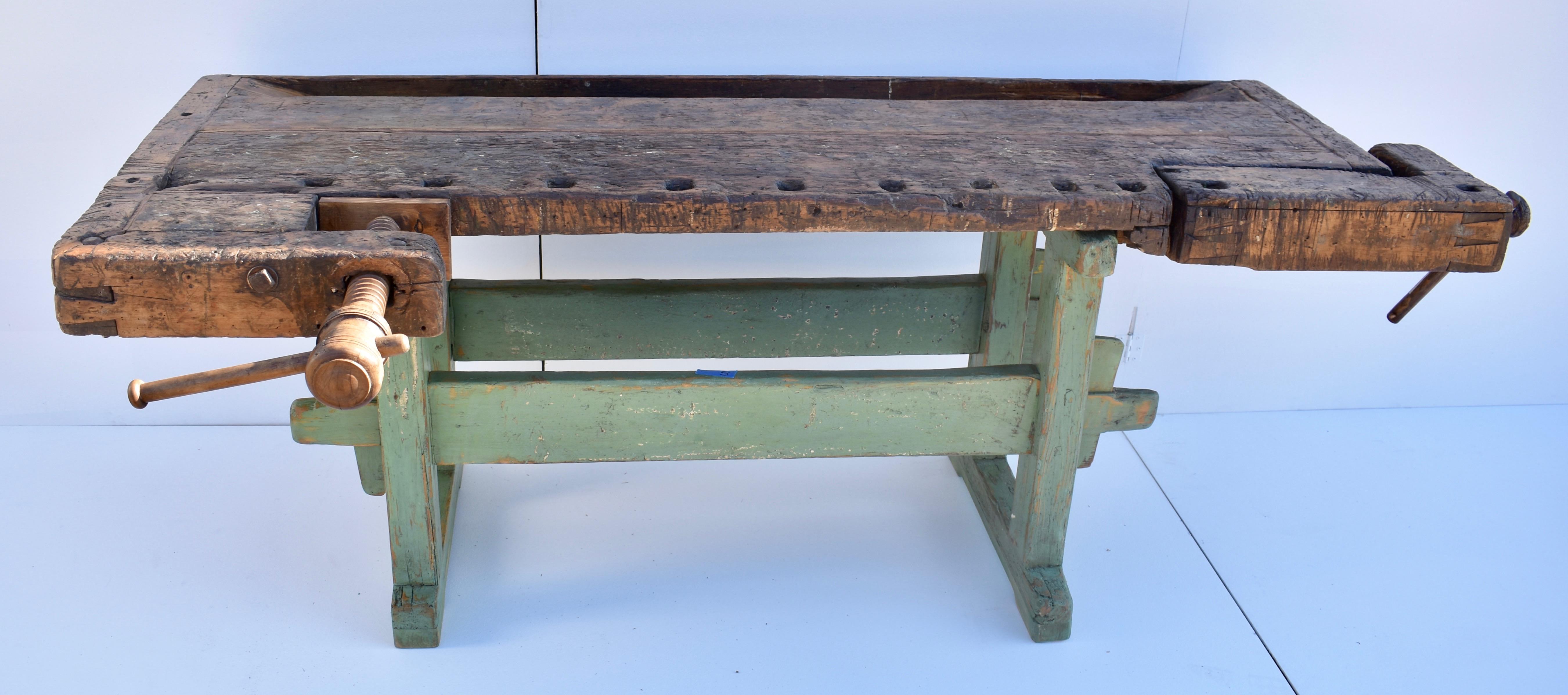 This superb antique carpenter’s bench is built as solid as a rock. The oak trestle-style base, painted green, has handcut members, through-tenoned and pegged together, the two ends joined by two 2” x 6” stretchers, and pulled tight on wooden keys.