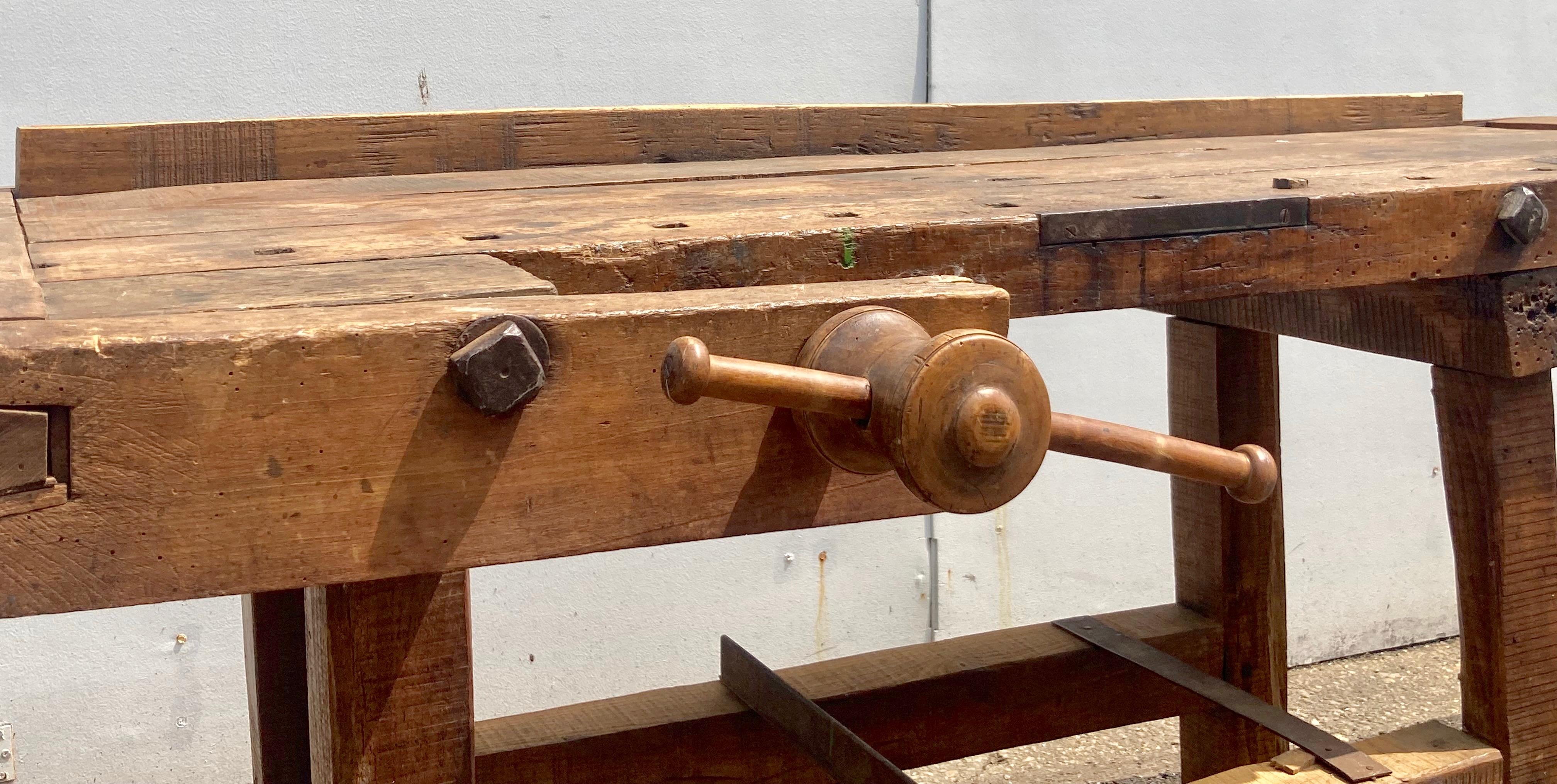 This beautifully naturally distressed carpenter’s workbench is unusual in that its base, made entirely of oak, is joined together in one piece.  Such benches usually have knock-down trestle-style bases.  It is a little harder to transport and